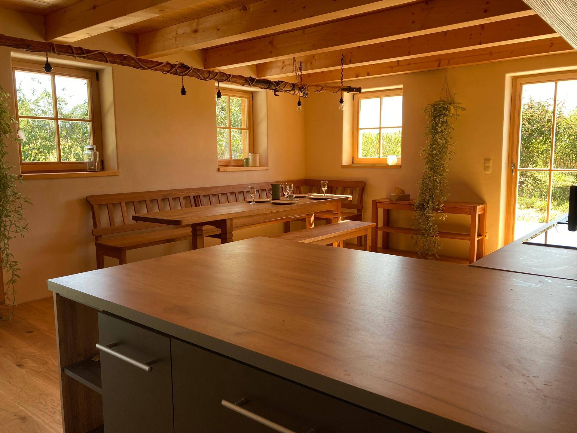 Gemütlicher Essbereich mit Holztisch und Bänken, umgeben von Fenstern mit Blick ins Grüne.