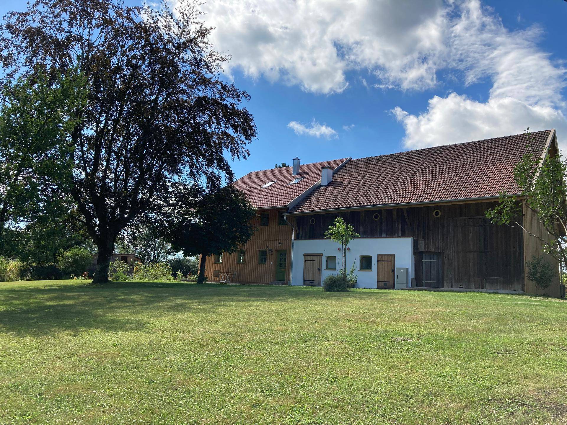 Ländliches Anwesen mit Holzhaus und angrenzendem Scheunengebäude, umgeben von Natur.