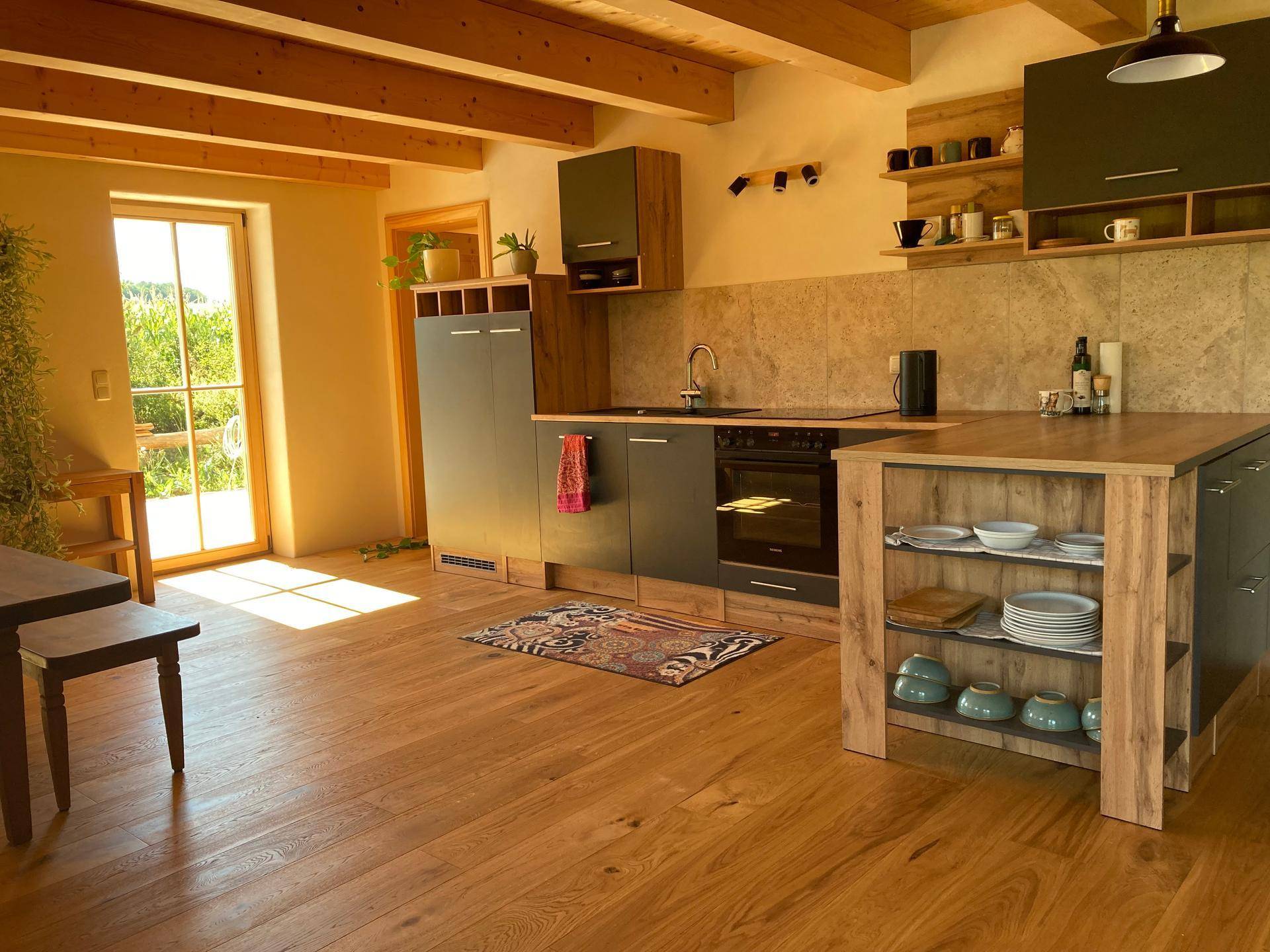 Moderne Einbauküche mit dunklen Fronten, Holztheke und Zugang zum Außenbereich.