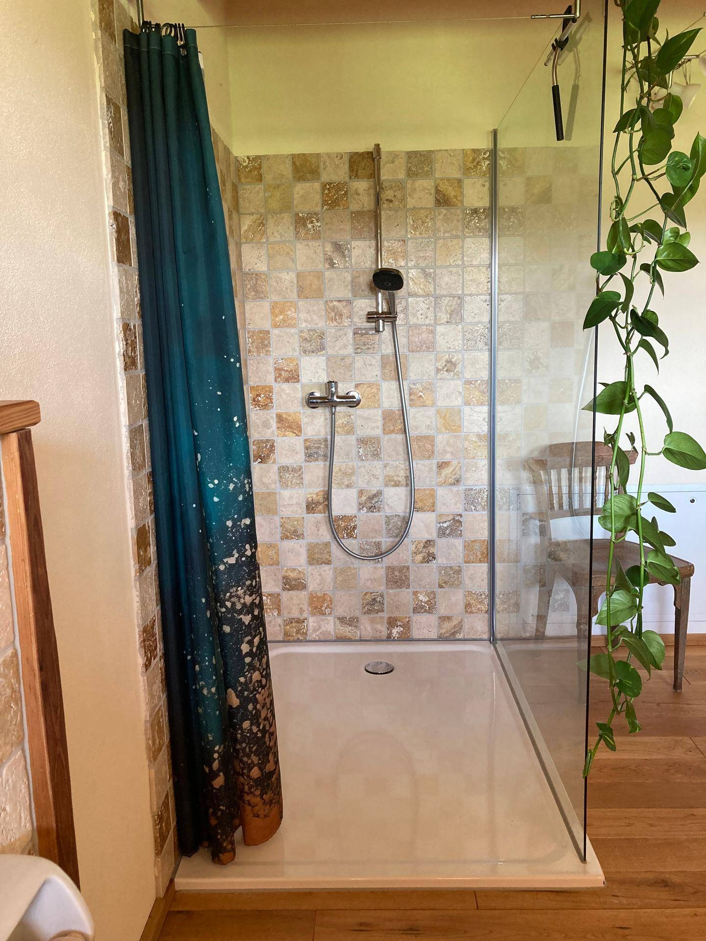 Moderne Dusche mit gemusterten Fliesen, Glaswand und Holzboden in einem hellen Bad.