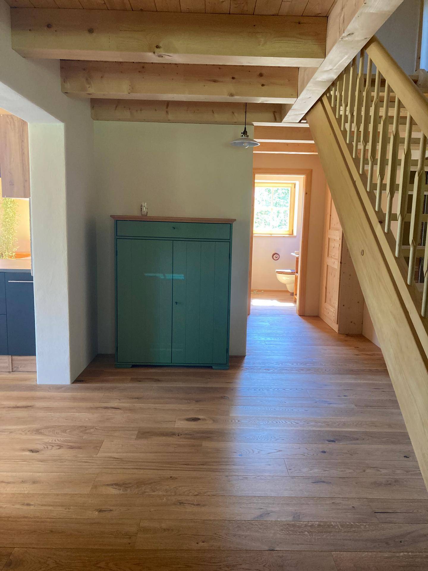 Eingangsbereich mit Holztreppe und grünem Schrank, der zu weiteren Räumen führt.