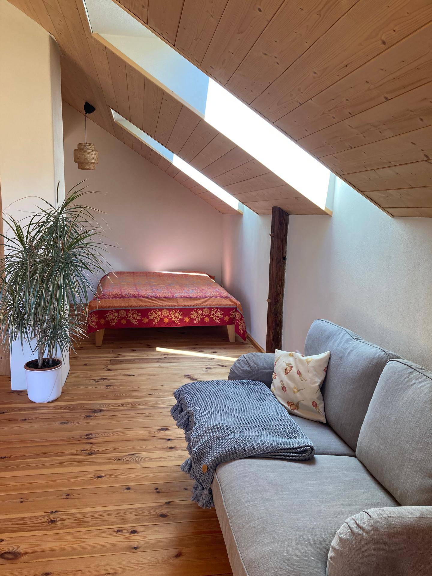 Helles Schlafzimmer mit Sofa, Holzboden und großem Dachfenster für viel Tageslicht.