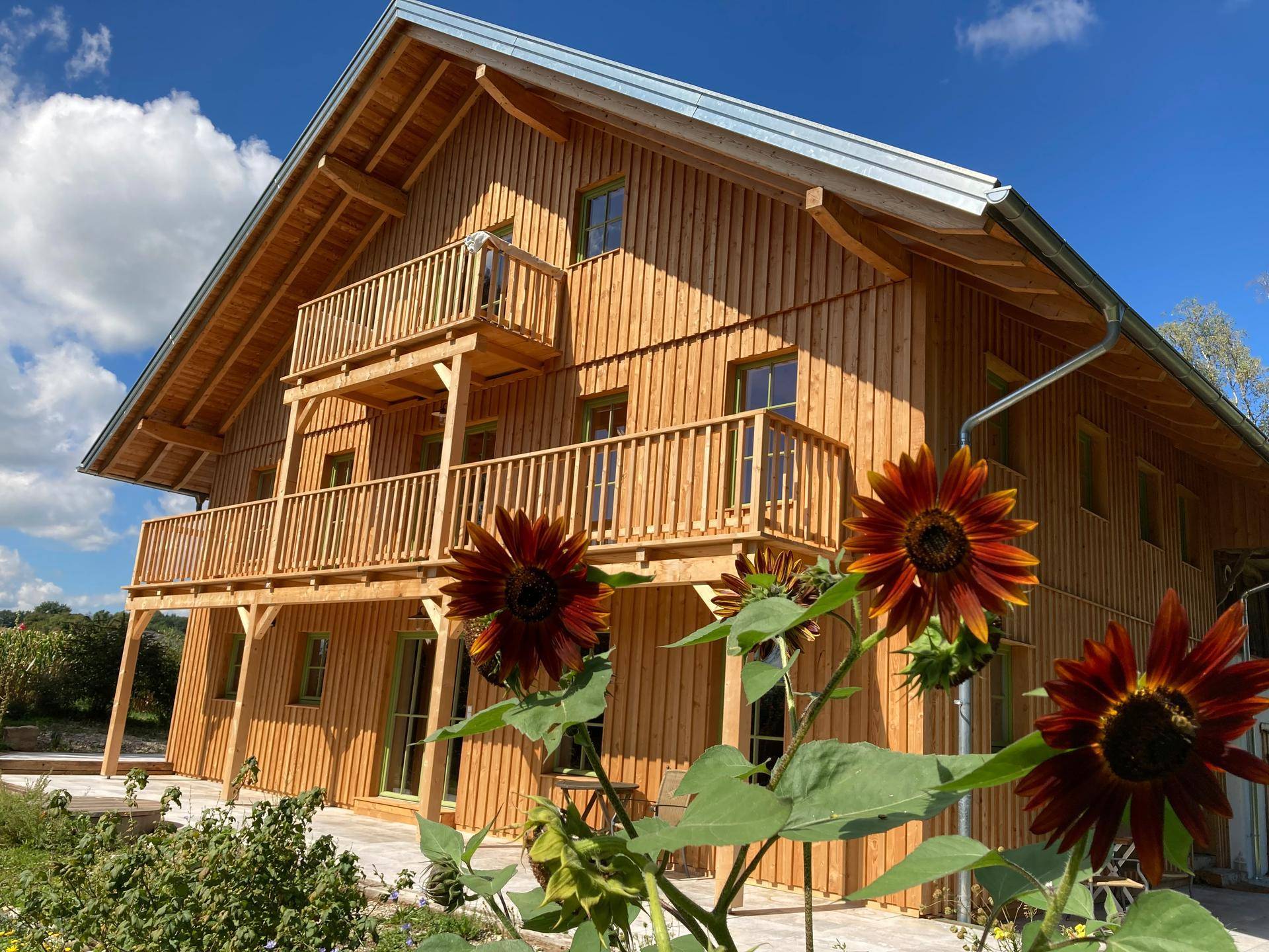 Sonnenblumen blühen vor der Holzfassade des Hauses mit seinen charmanten Balkonen.