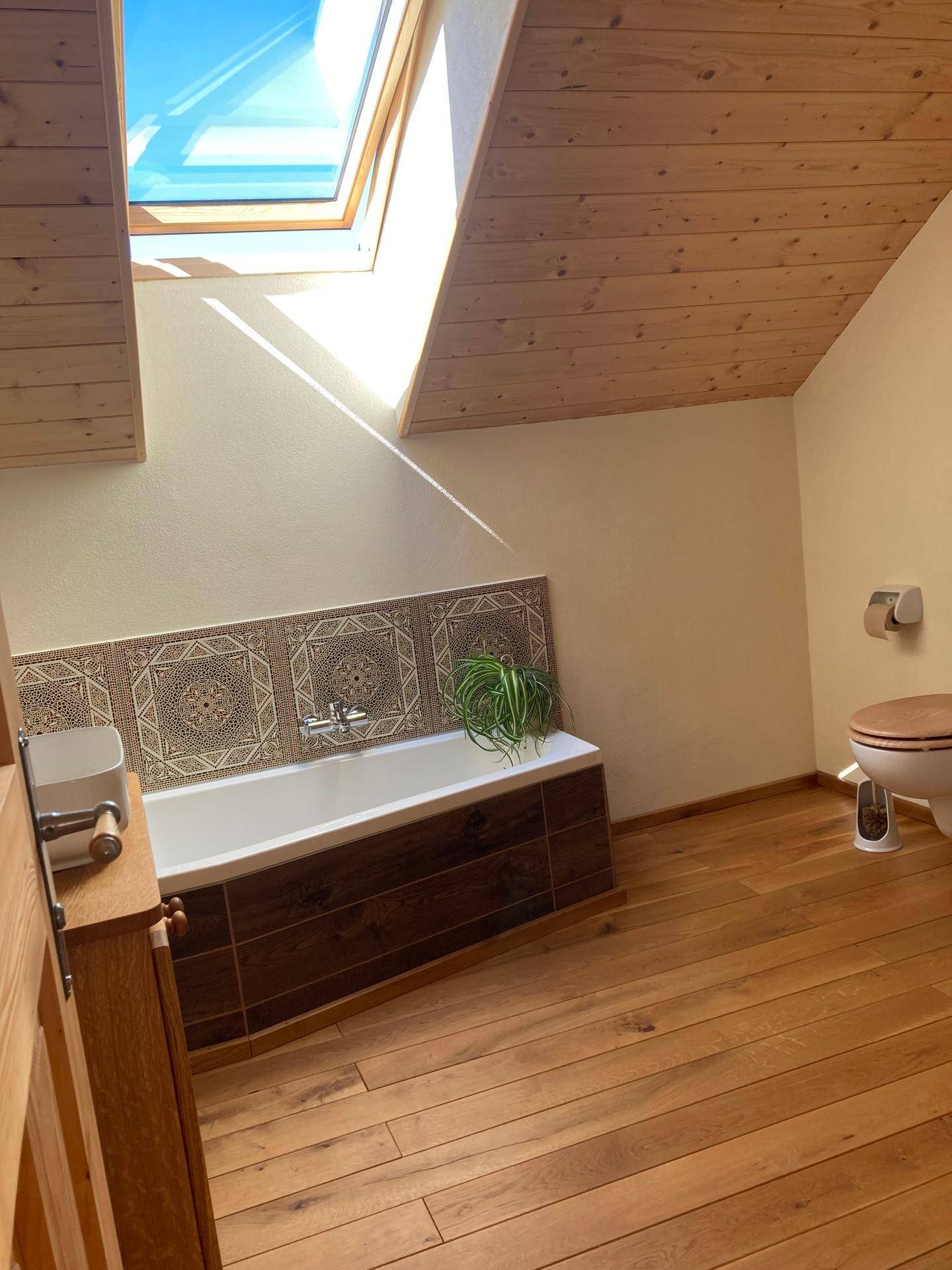 Badezimmer mit Badewanne, Toilette und Dachfenster für viel Tageslicht.