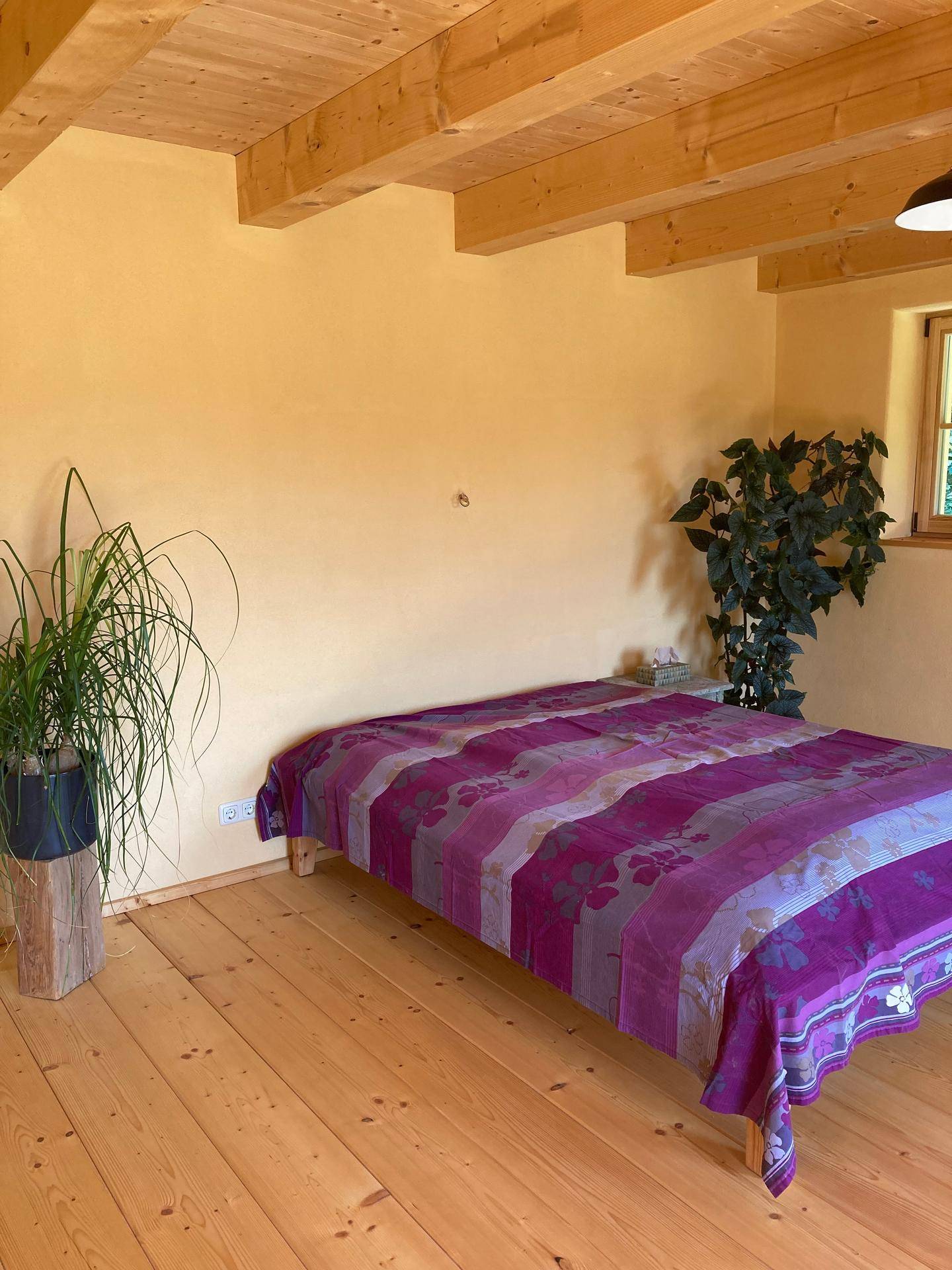 Schlafzimmer mit Holzdielenboden, gelben Wänden und einem großen Bett.