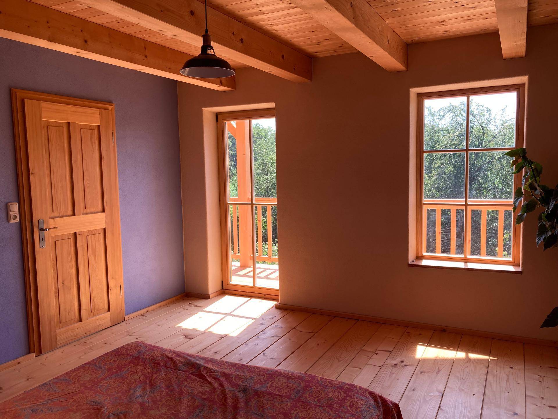 Schlafzimmer mit Holzdielenboden, Holztüren und Zugang zu einem weiteren Raum oder Balkon.
