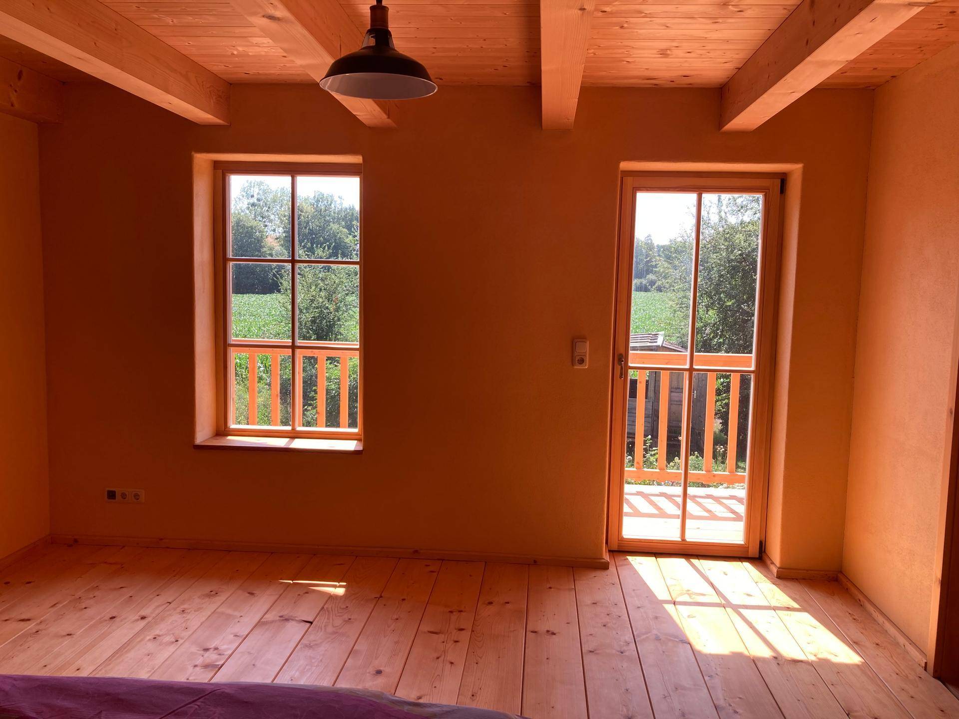Schlafzimmer mit Holzdielenboden, gelben Wänden und Zugang zu einem Balkon.