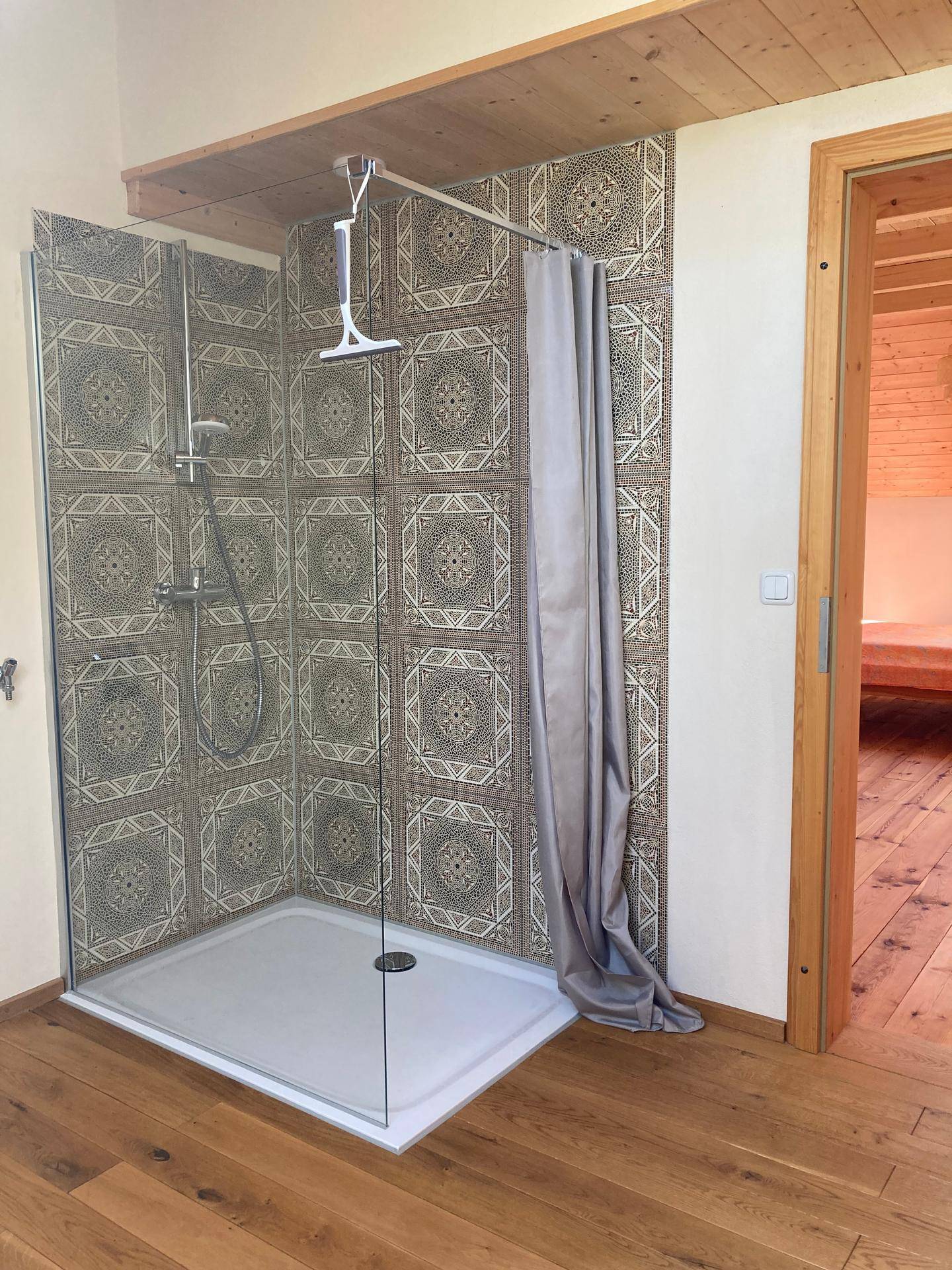 Moderne Dusche mit gemusterten Fliesen, Glaswand und Holzboden in einem hellen Bad.
