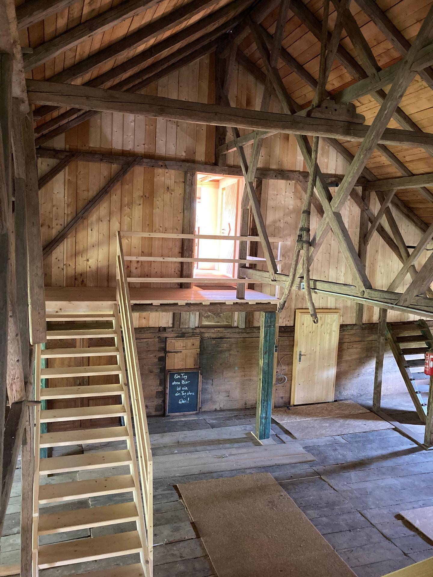 Dachboden mit Holztreppe und Zwischenebene, die viel natürliches Licht durch eine Öffnung erhält.