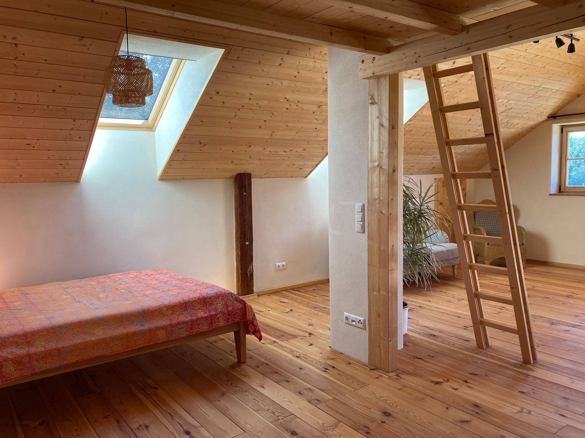Gemütliches Schlafzimmer mit Holzboden, Dachschrägen und einem hellen Dachfenster.
