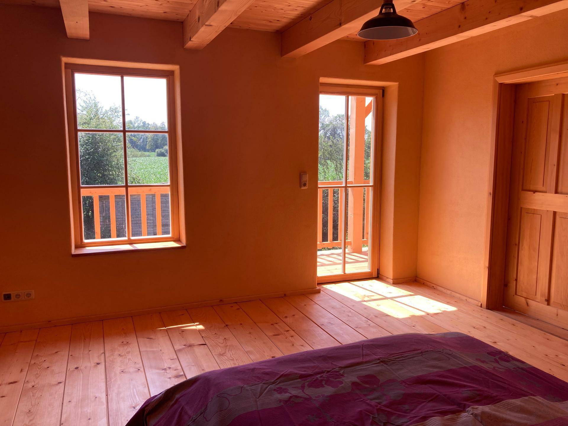Schlafzimmer mit Holzdielenboden, gelben Wänden und Zugang zu einem Balkon.