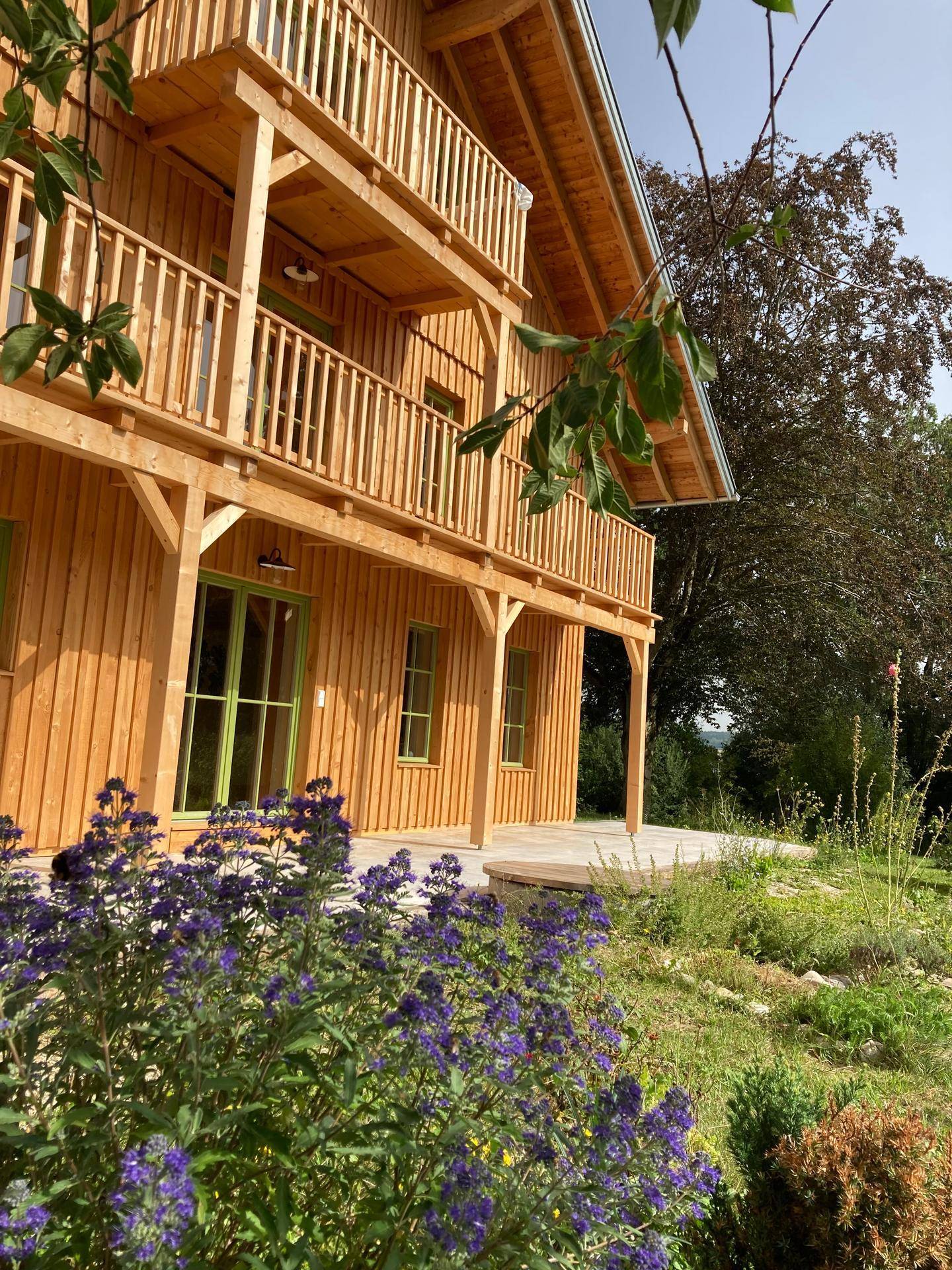 Lila Blüten im Vordergrund vor der Holzfassade des Hauses mit Balkonen und Terrasse.