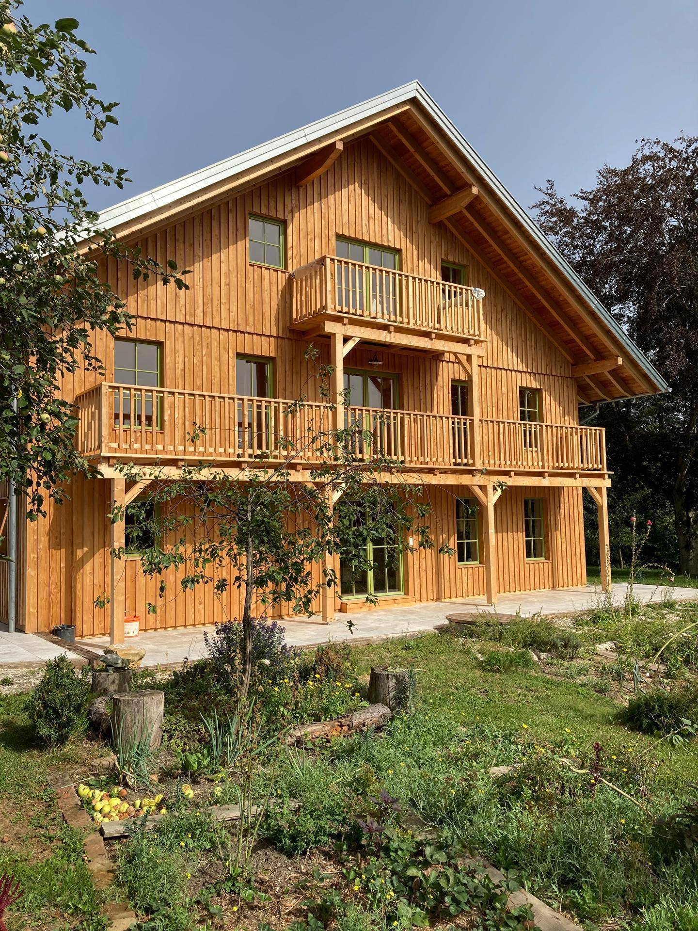 Seitenansicht des Holzhauses mit Balkonen und einem naturnahen Gartenbereich.