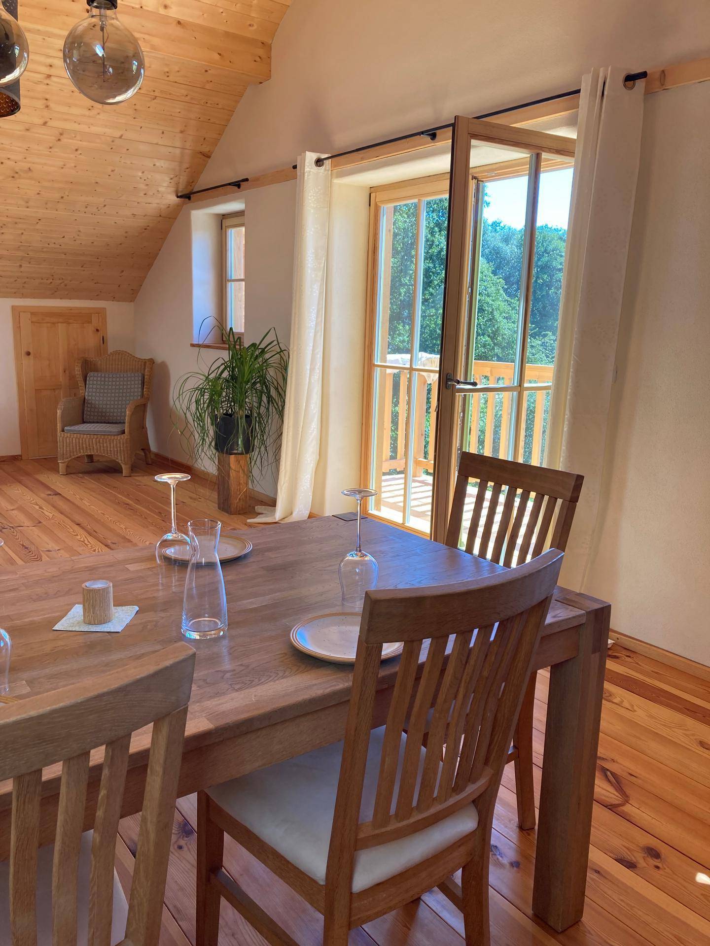 Heller Essbereich mit Holztisch und Zugang zu einem Balkon, der einen grünen Ausblick bietet.