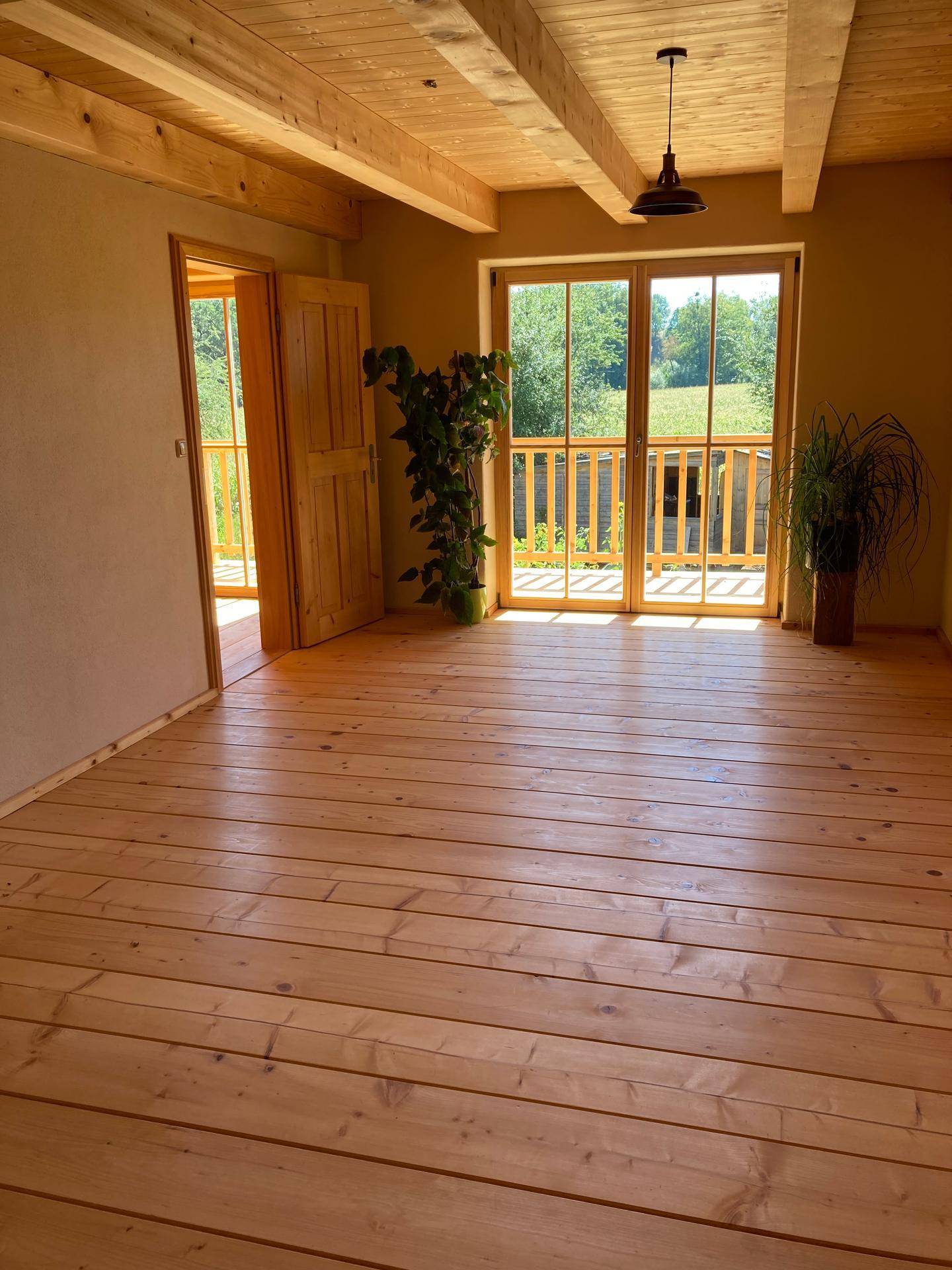 Helles Schlafzimmer mit Holzdielenboden, Holzbalkendecke und Zugang zum Balkon.