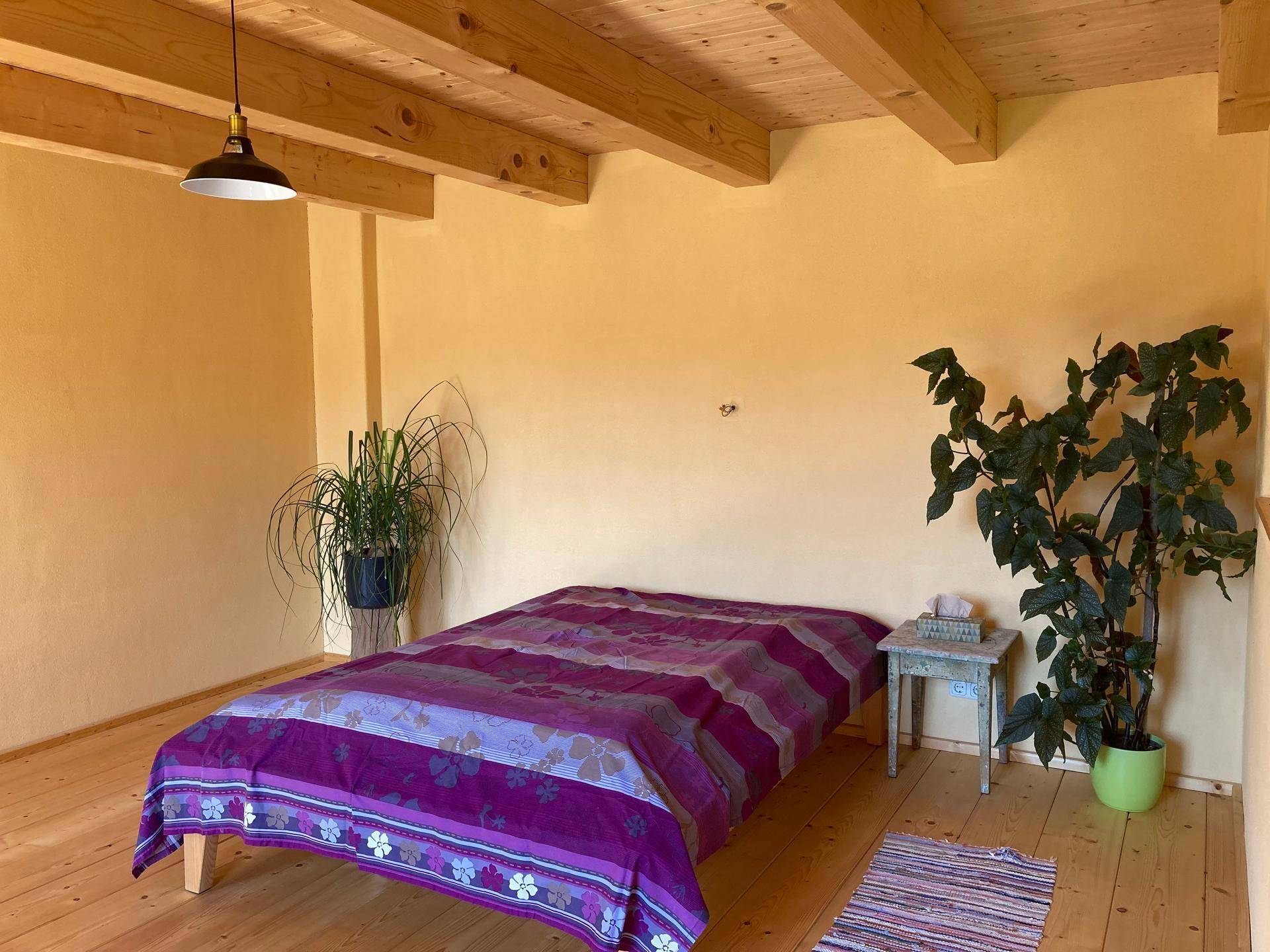 Schlafzimmer mit Holzdielenboden, gelben Wänden und einem großen Bett.