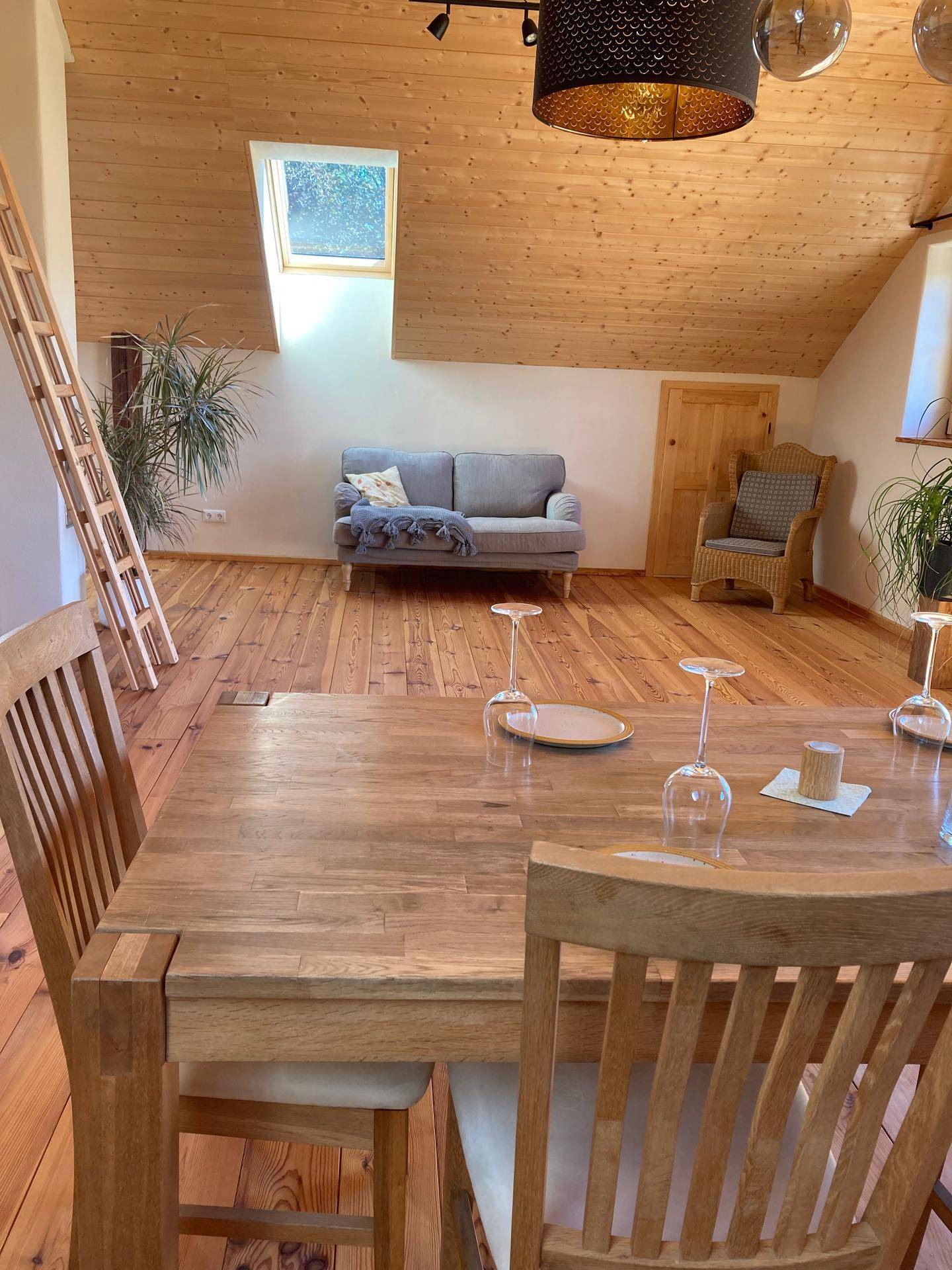 Gemütlicher Wohn- und Essbereich mit Holzboden, Dachschräge, Sofa und einem Dachfenster für natürliches Licht.