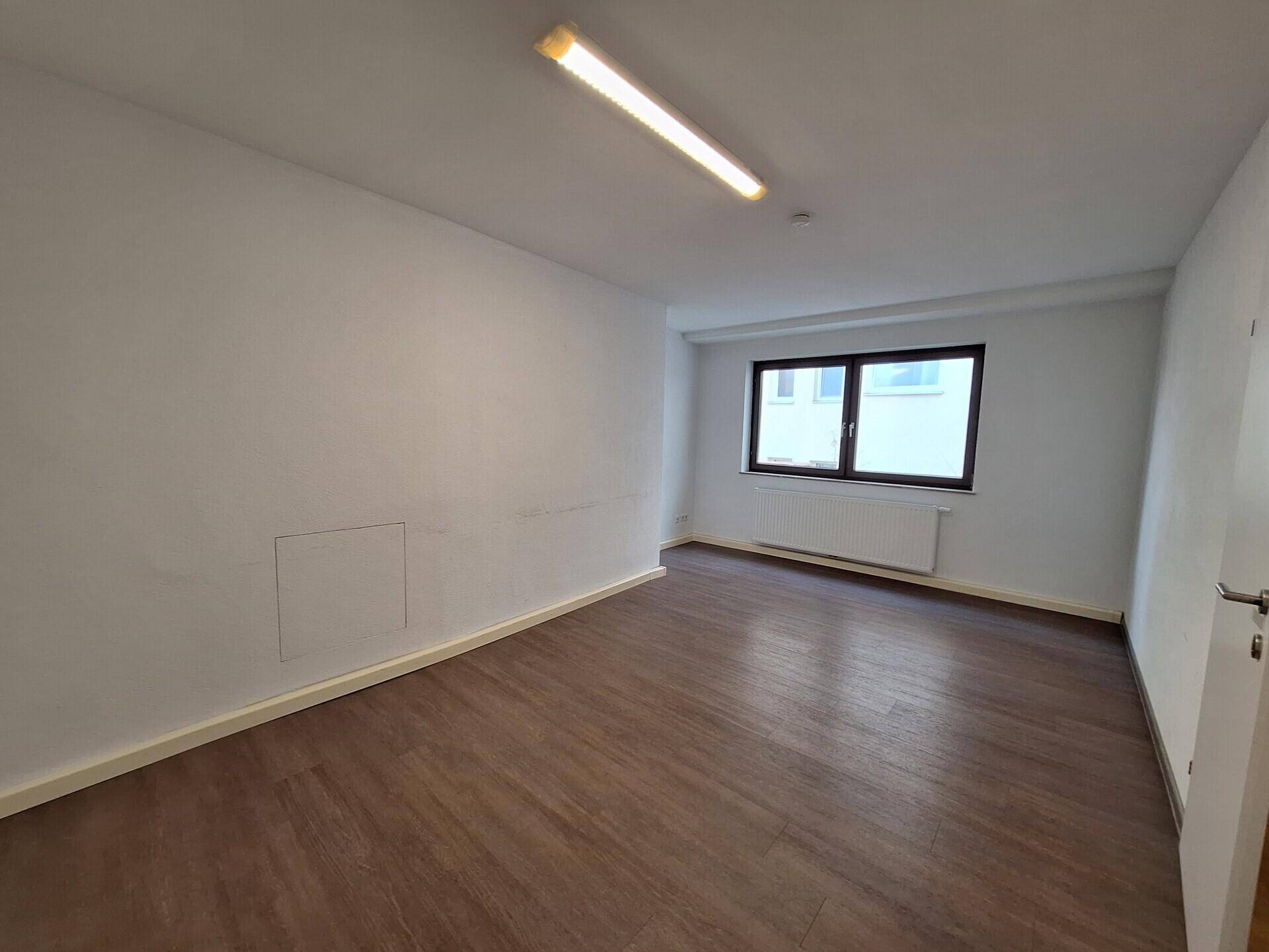 Helles Zimmer mit Laminatboden, weißen Wänden und großem Fenster, ideal als Schlaf- oder Arbeitszimmer.