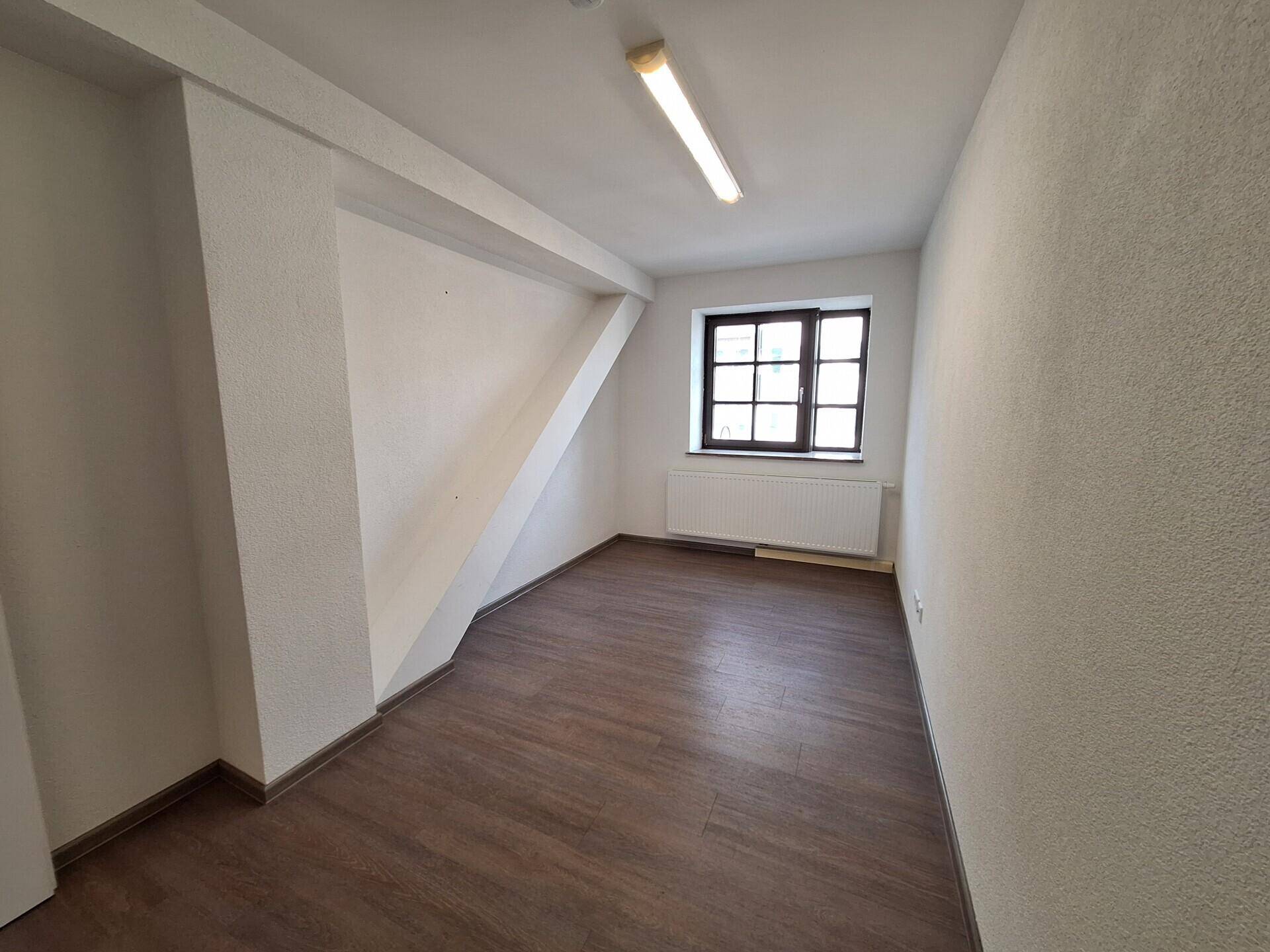 Zimmer mit Laminatboden, weißen Wänden und schrägen Elementen, bietet vielseitige Nutzungsmöglichkeiten.