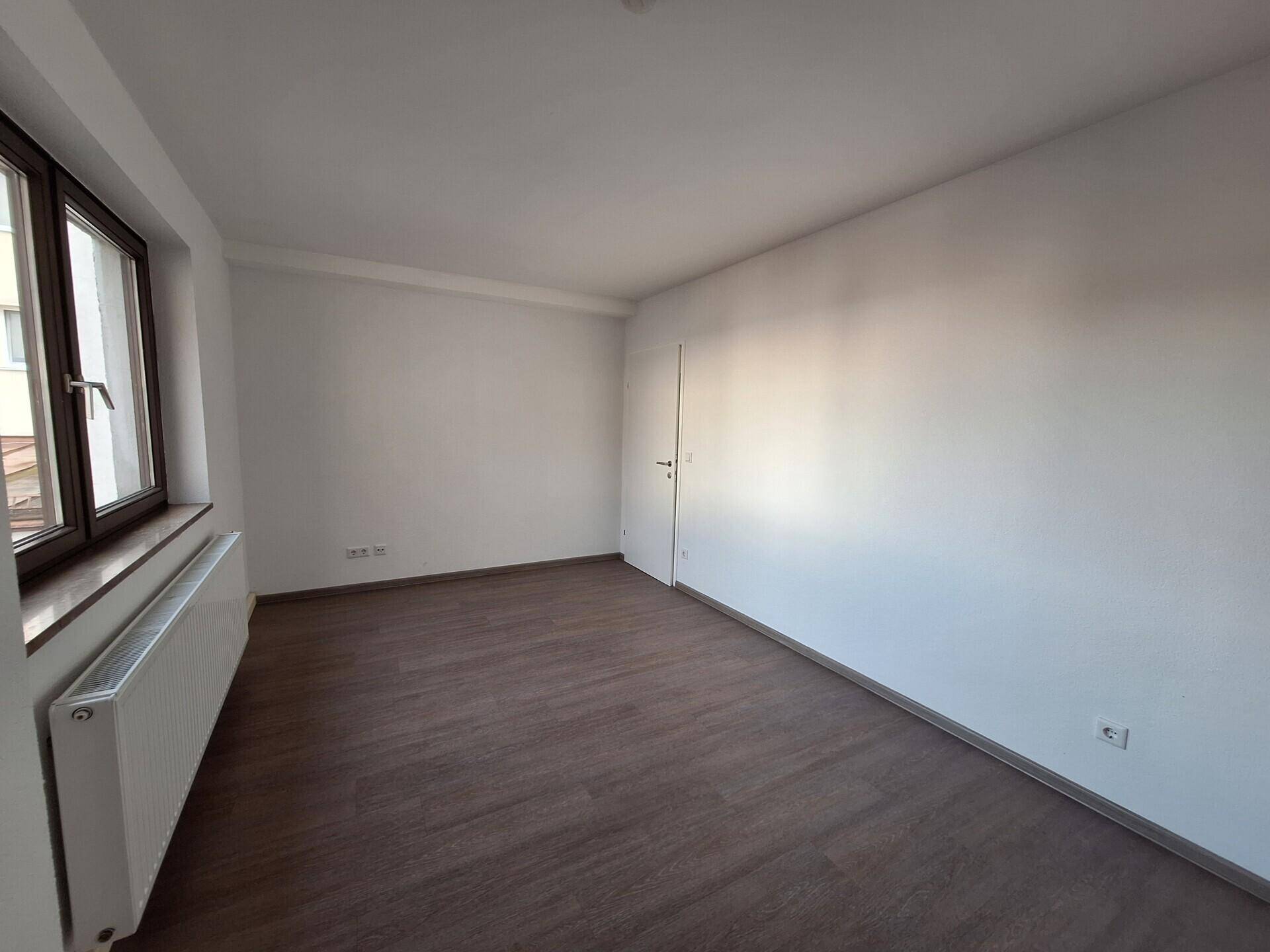 Leeres Zimmer mit Laminatboden, weißen Wänden und Fenster für individuelle Gestaltungsmöglichkeiten.
