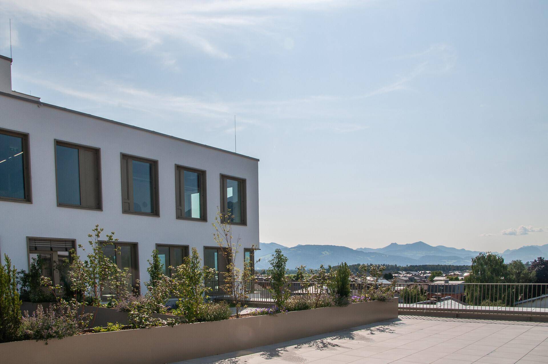Helle Dachterrasse mit modernen Pflanzgefäßen und einem Panoramablick über die Stadt und die Berge.