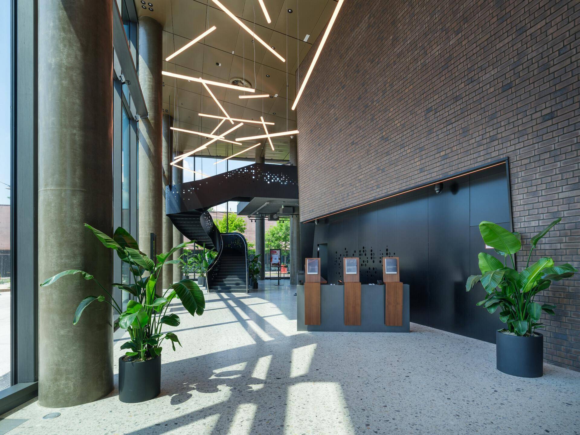 Elegante, moderne Lobby mit hohen Decken, großen Fenstern, Wendeltreppe und stilvoller Beleuchtung.