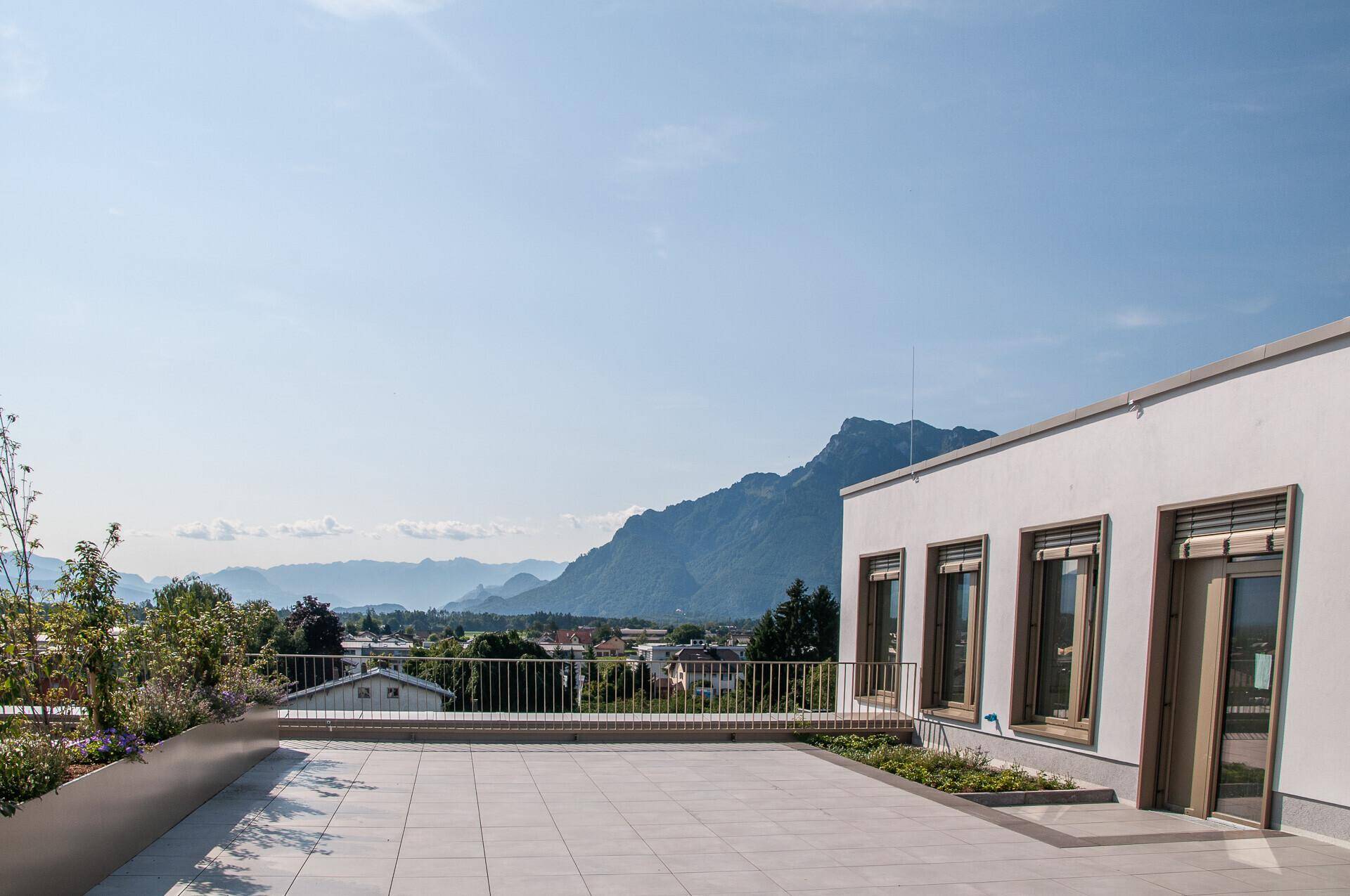 Geräumige Dachterrasse mit Fliesenboden, Pflanzenkübeln und einem weiten Blick auf die umliegende Berglandschaft.