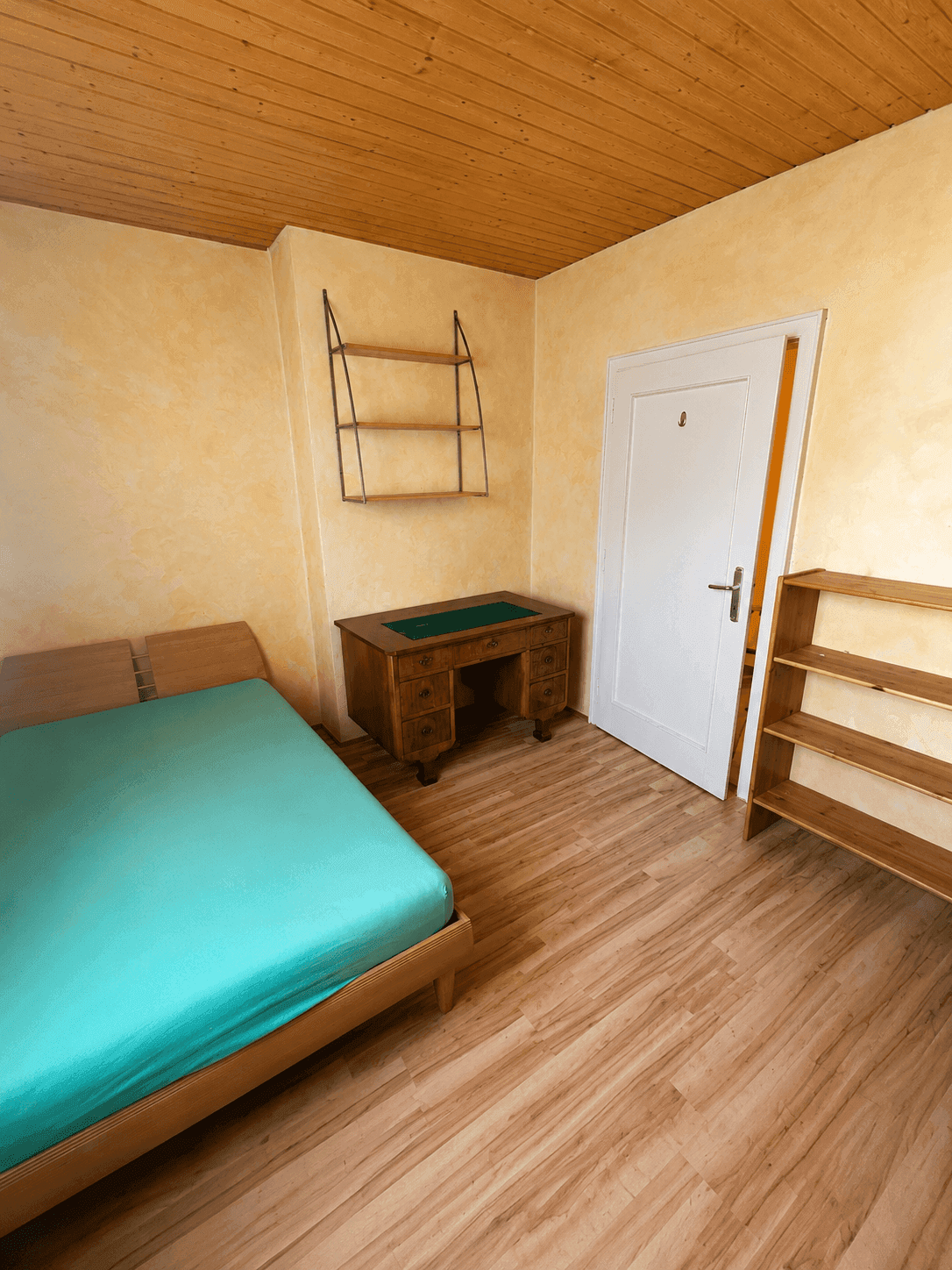 Schlafzimmer mit Holzbett, antikem Schreibtisch und Holzdecke in warmen Farbtönen.