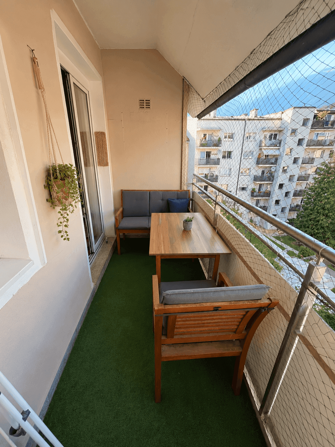 Gemütlicher Balkon mit Kunstrasen, Gartenmöbeln und Blick auf umliegende Gebäude.