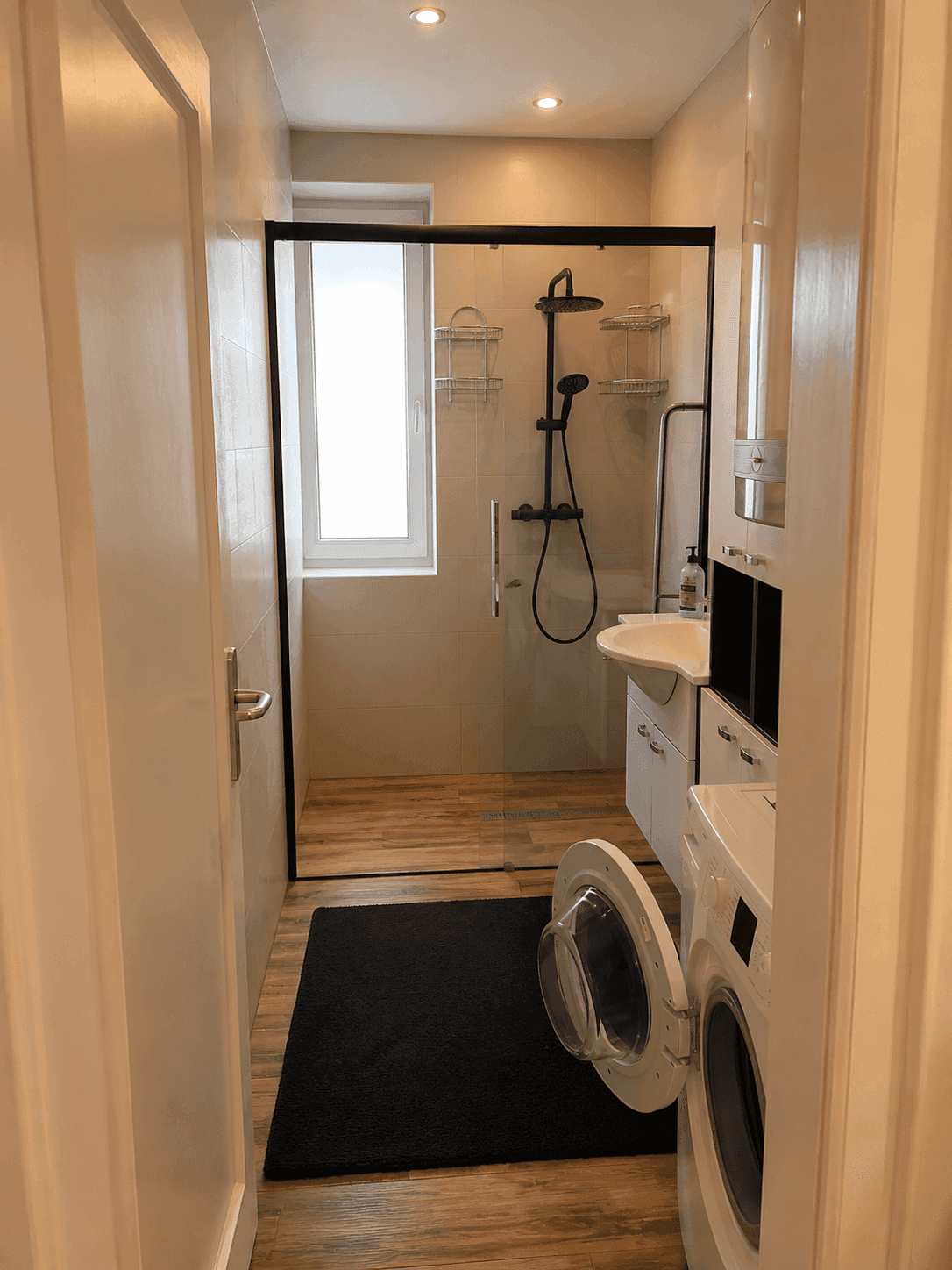Modernes Badezimmer mit ebenerdiger Dusche, Waschbecken, WC und Waschmaschine.