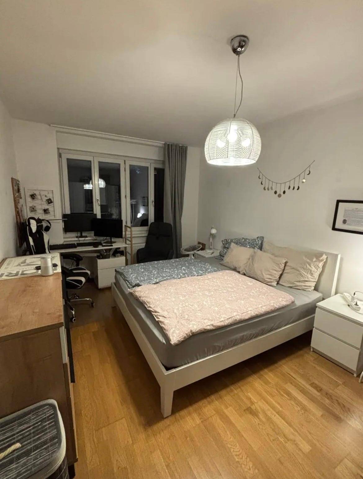 Gemütliches Schlafzimmer mit Holzboden, großem Fenster und Arbeitsbereich.