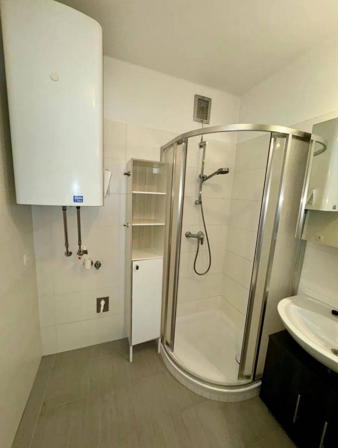 Badezimmer mit Duschkabine, Waschbecken und Warmwasserboiler.