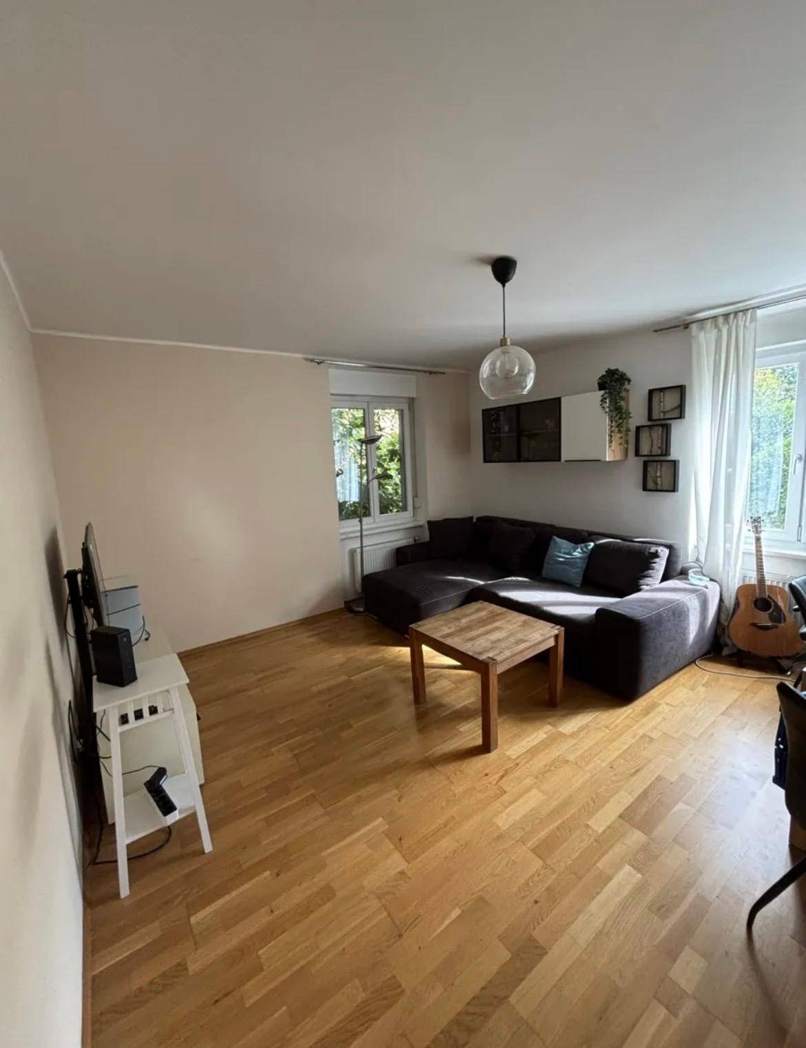 Geräumiges Wohnzimmer mit Holzboden, großem Sofa und viel Tageslicht.