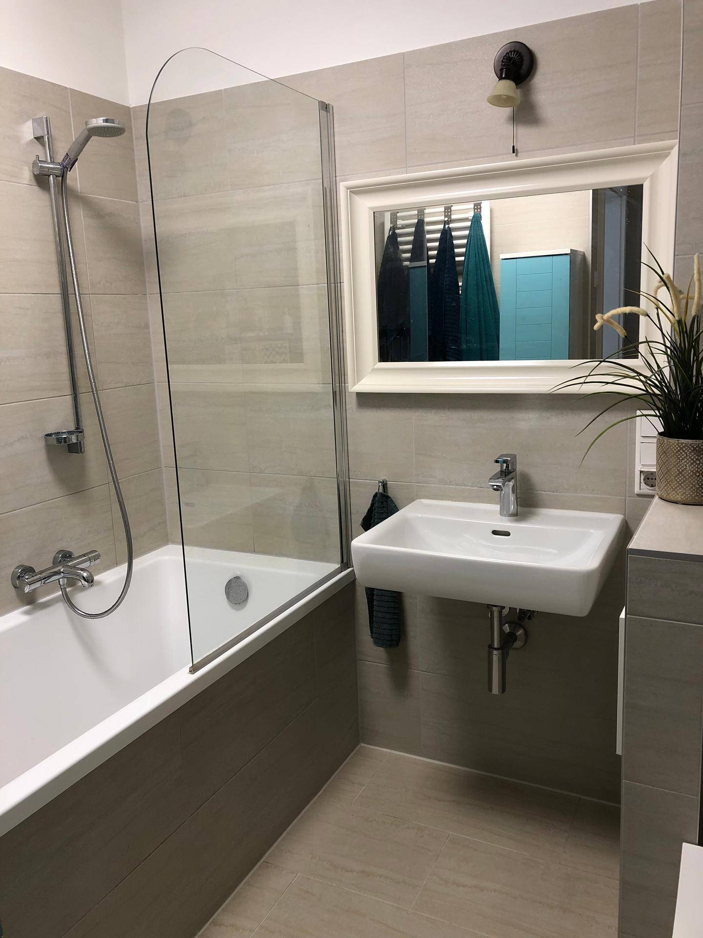 Modernes Badezimmer mit Badewanne, Duschwand, Einzelwaschbecken und hellen Fliesen.