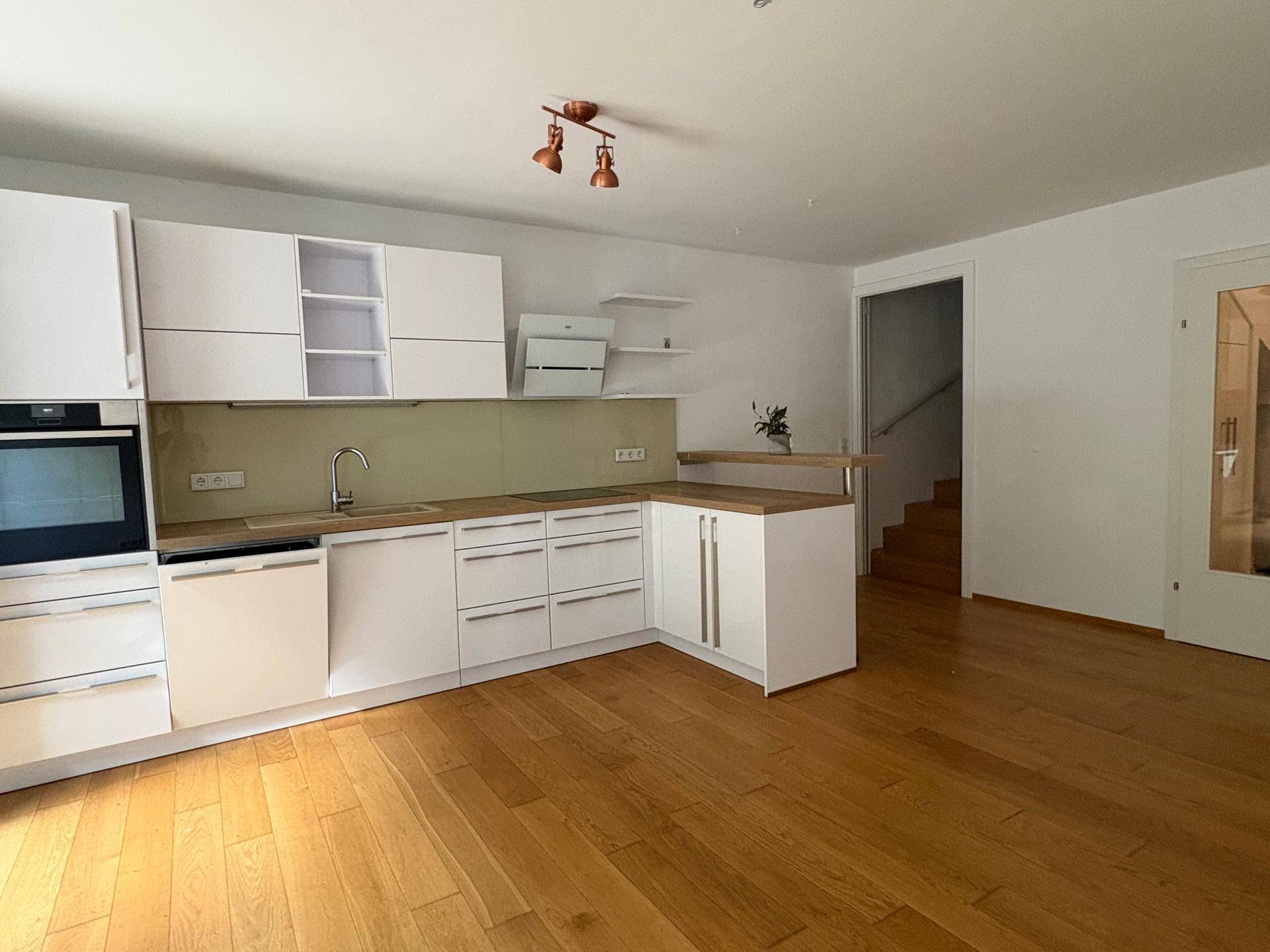 Funktionale Einbauküche mit Holztheke, weißen Schränken und Treppenaufgang im Hintergrund.