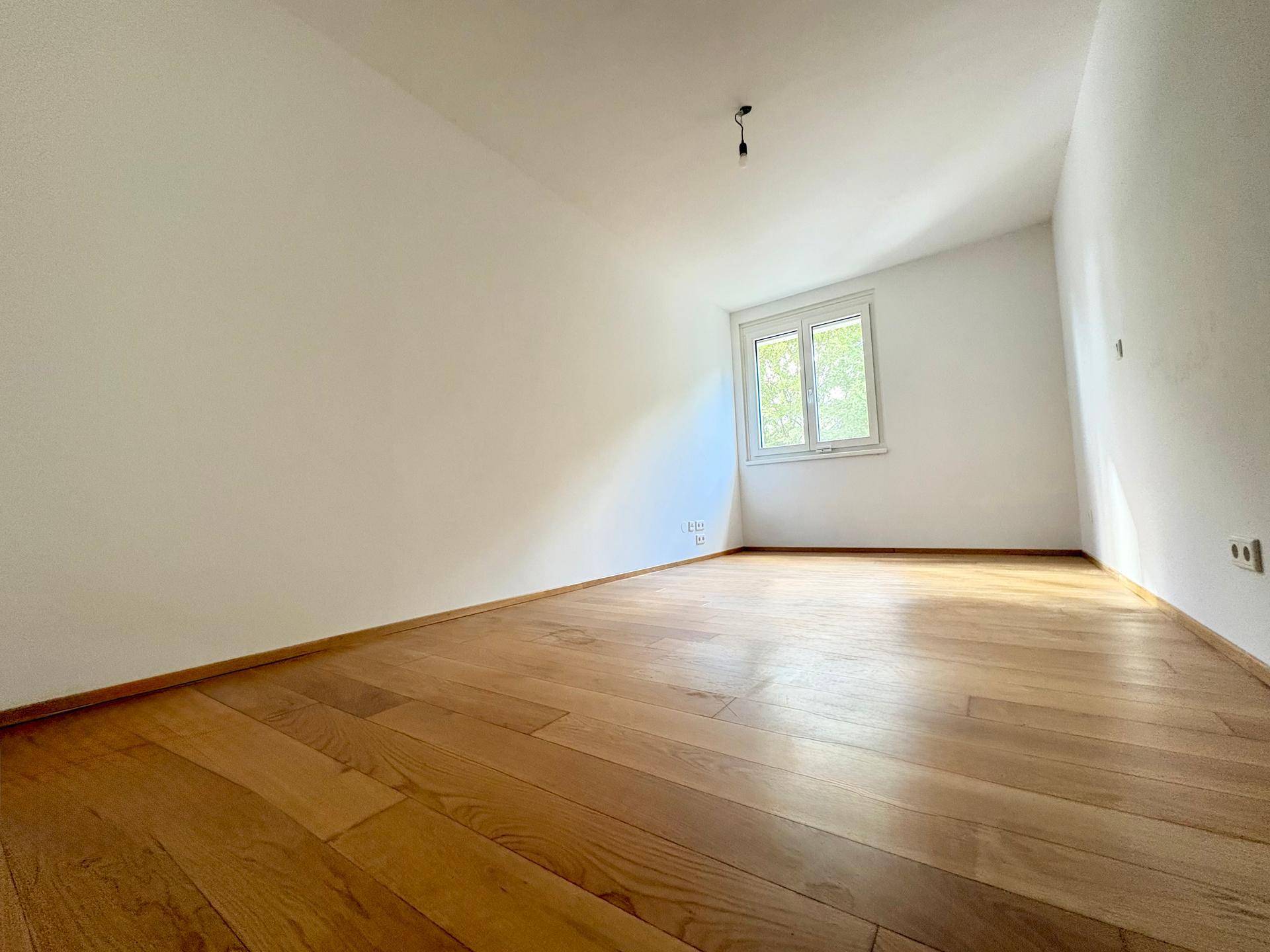 Geräumiges Zimmer mit Holzboden, charakteristischer Dachschräge und Fenster für natürliches Licht.