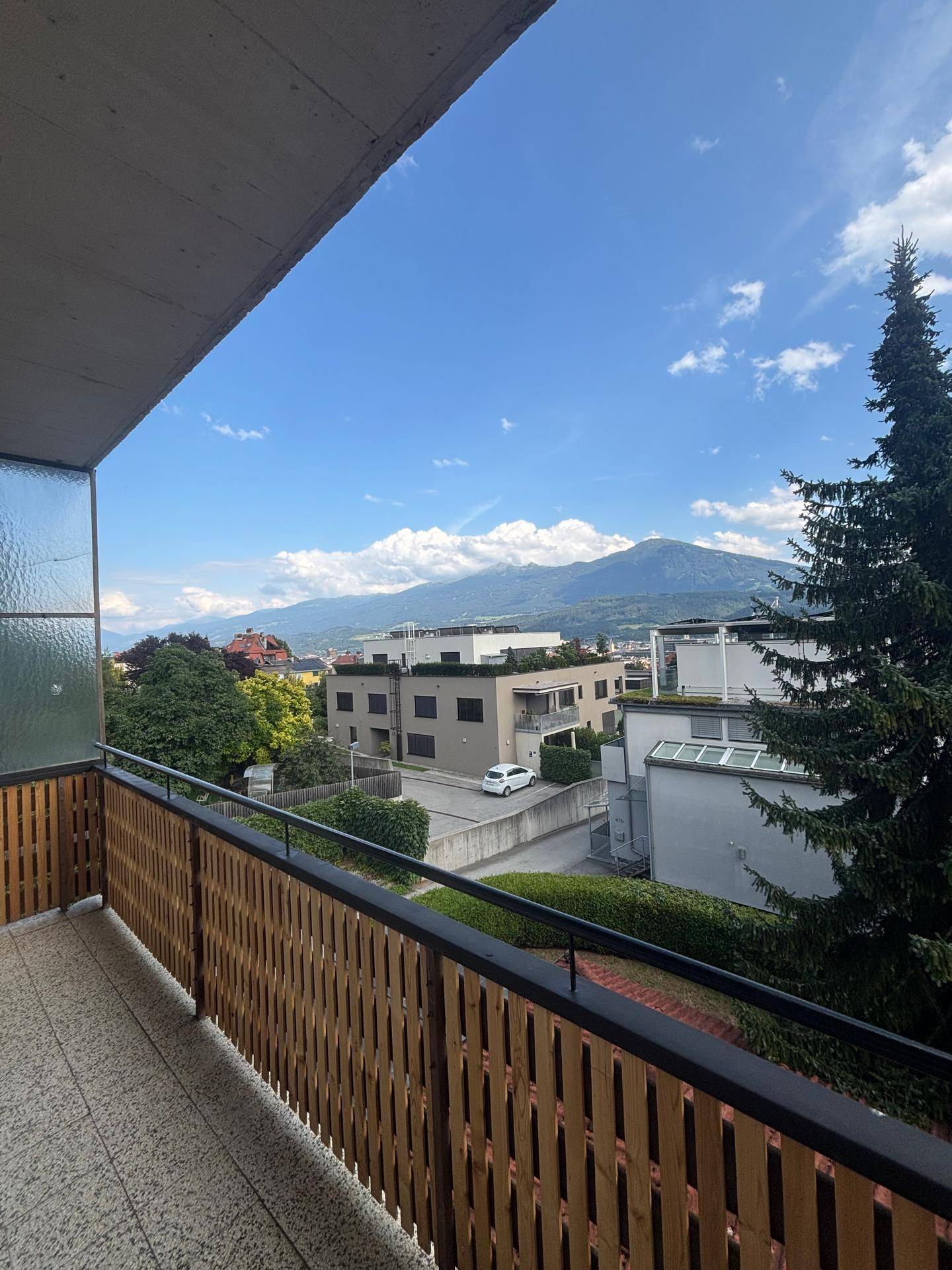 Geräumiger Balkon mit Holzbalkonbrüstung, Fliesenboden und einem weiten Blick auf die Berge.