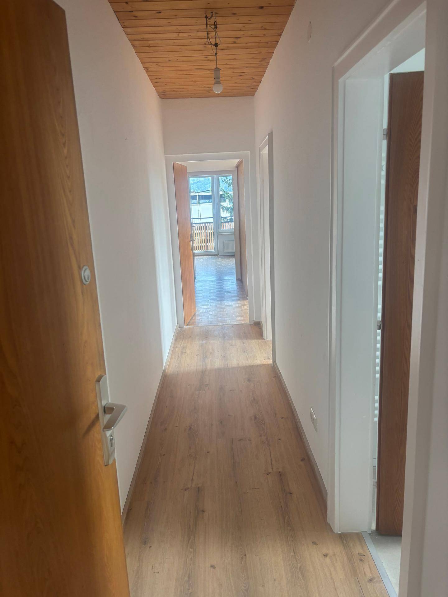 Heller Flur mit Laminatboden und Holzdecke, der zu weiteren Zimmern und einem Balkon führt.