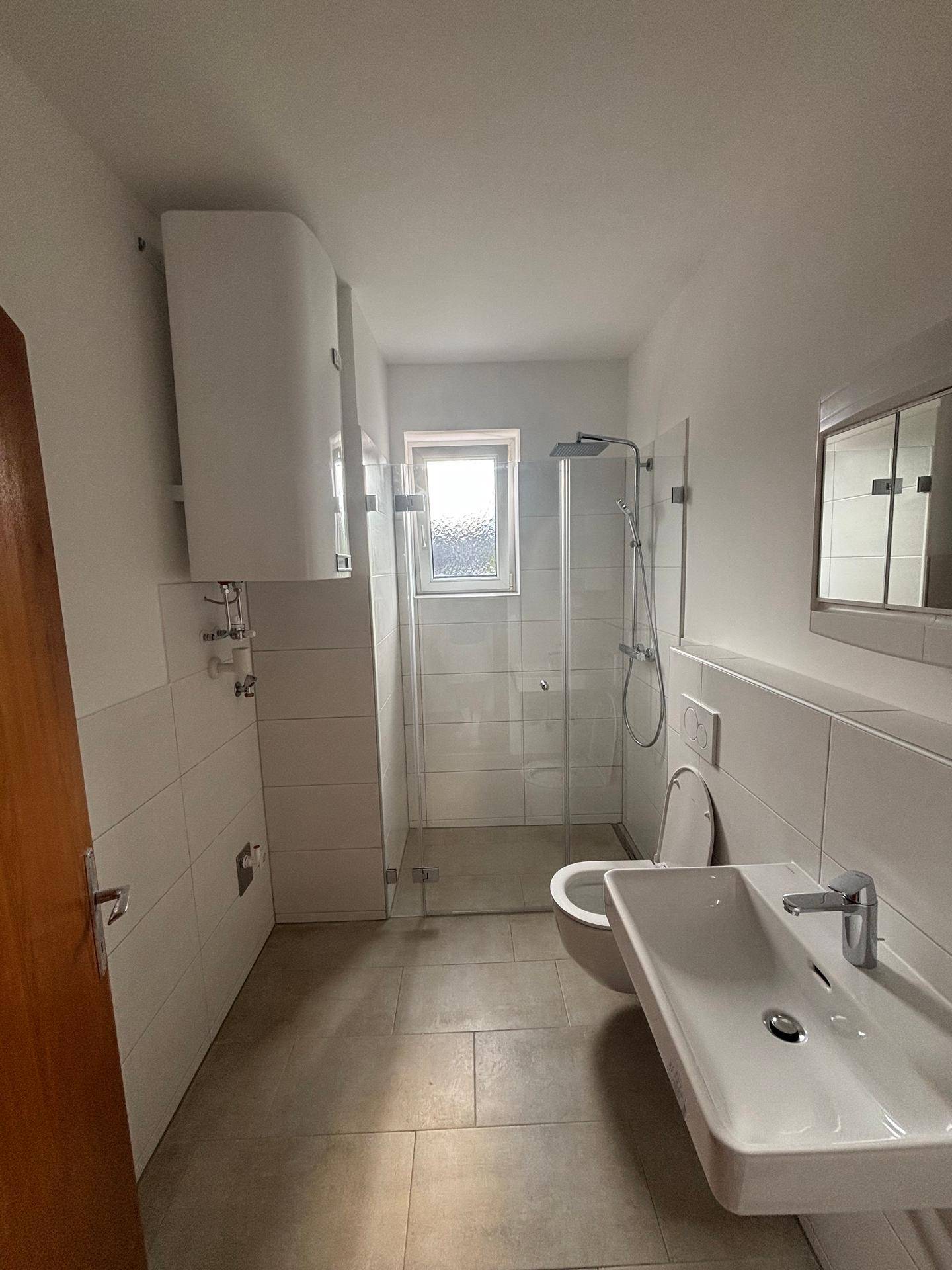 Modernes Badezimmer mit weißen Fliesen, ebenerdiger Dusche, WC, Waschbecken und einem kleinen Fenster.
