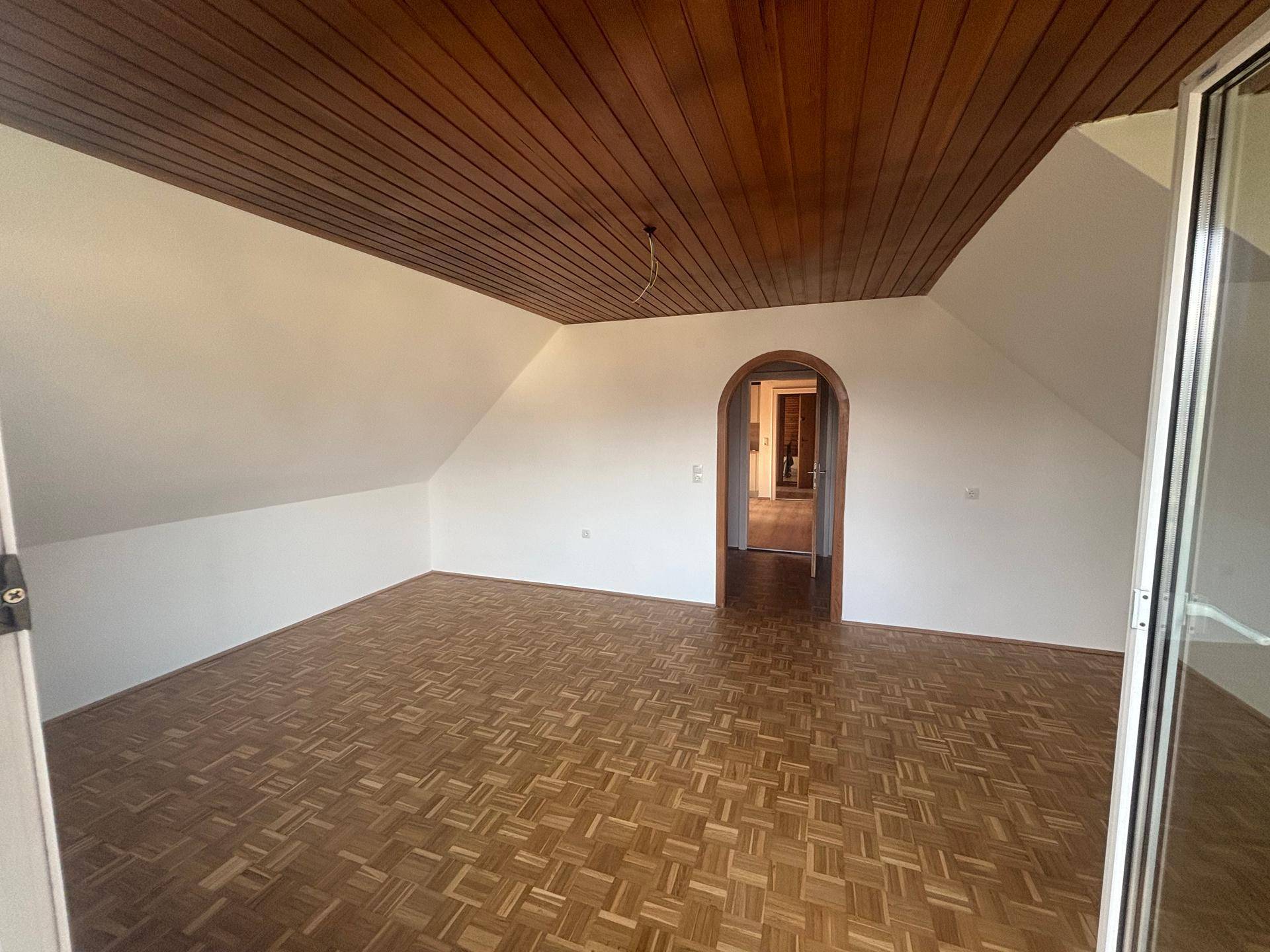 Geräumiges Zimmer mit Parkettboden, Holzbalkendecke und Dachschrägen, ideal als Schlafzimmer.