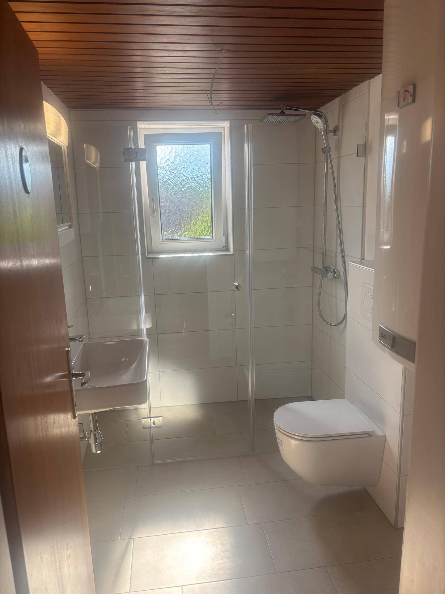 Modernes Badezimmer mit begehbarer Dusche, wandhängendem WC und Fenster für Tageslicht.