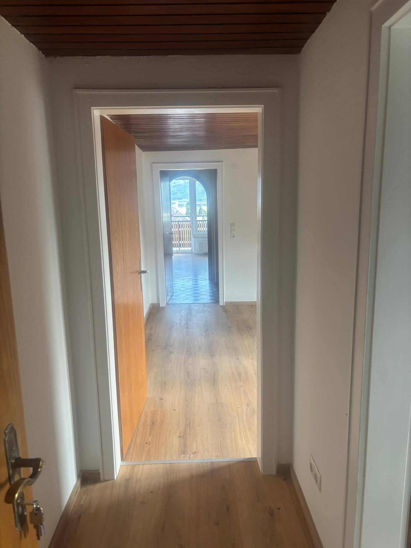 Heller Flur mit Laminatboden und Holzbalkendecke, der zu weiteren Räumen führt.