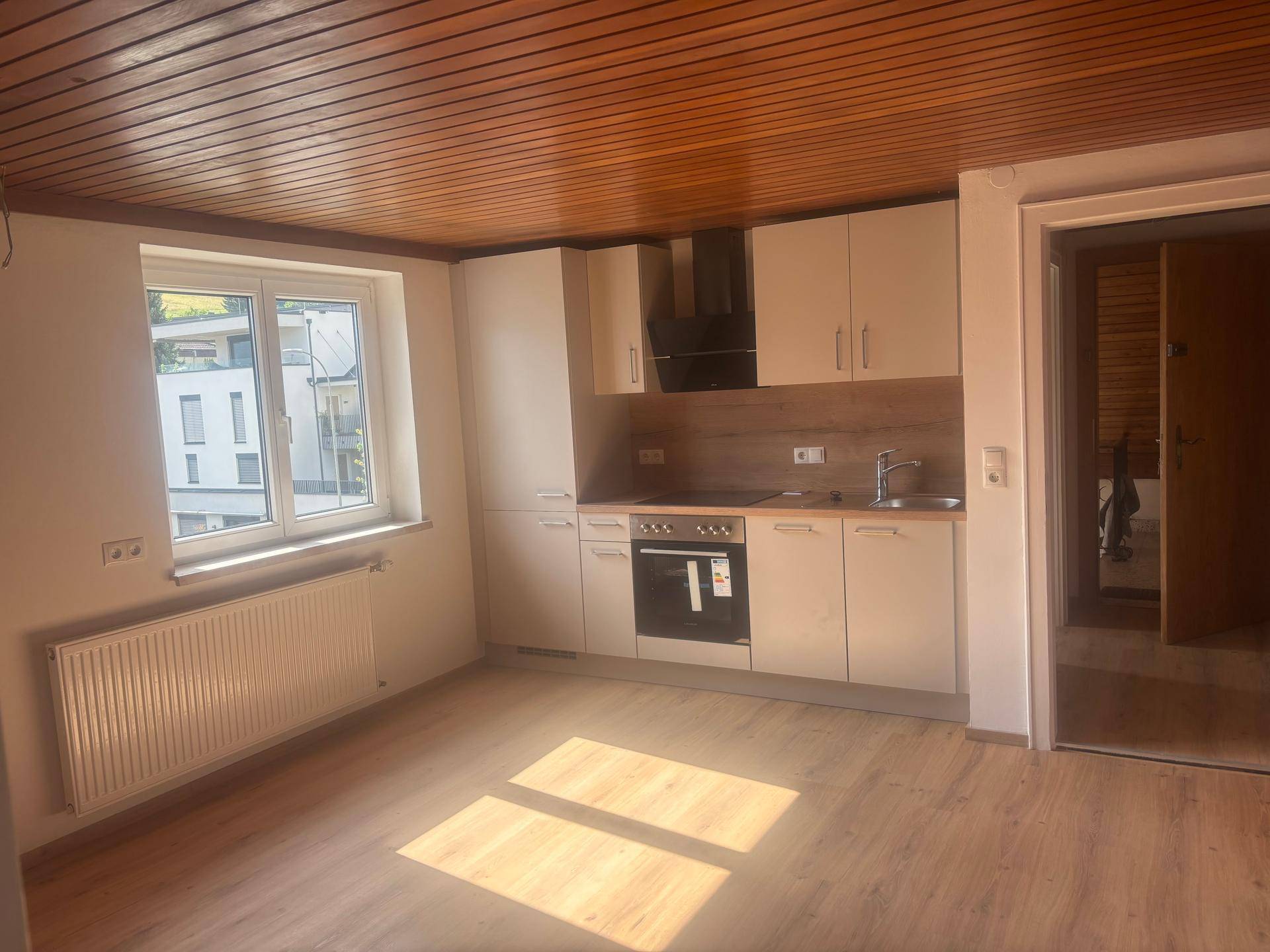 Moderne Einbauküche mit hellen Schränken, integriertem Backofen und Holzbalkendecke.
