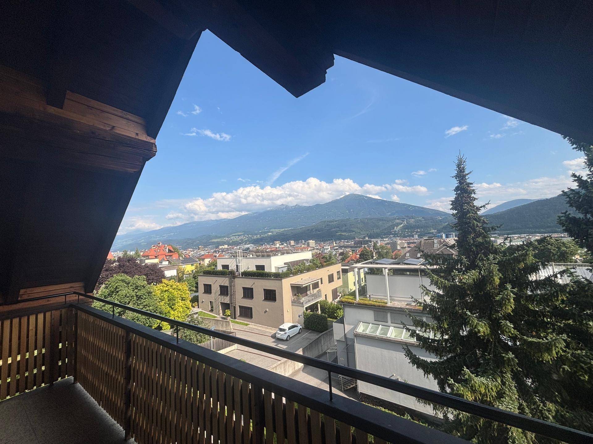 Geräumiger Balkon mit Holzbalken und Panoramablick auf die Stadt und die umliegenden Berge.