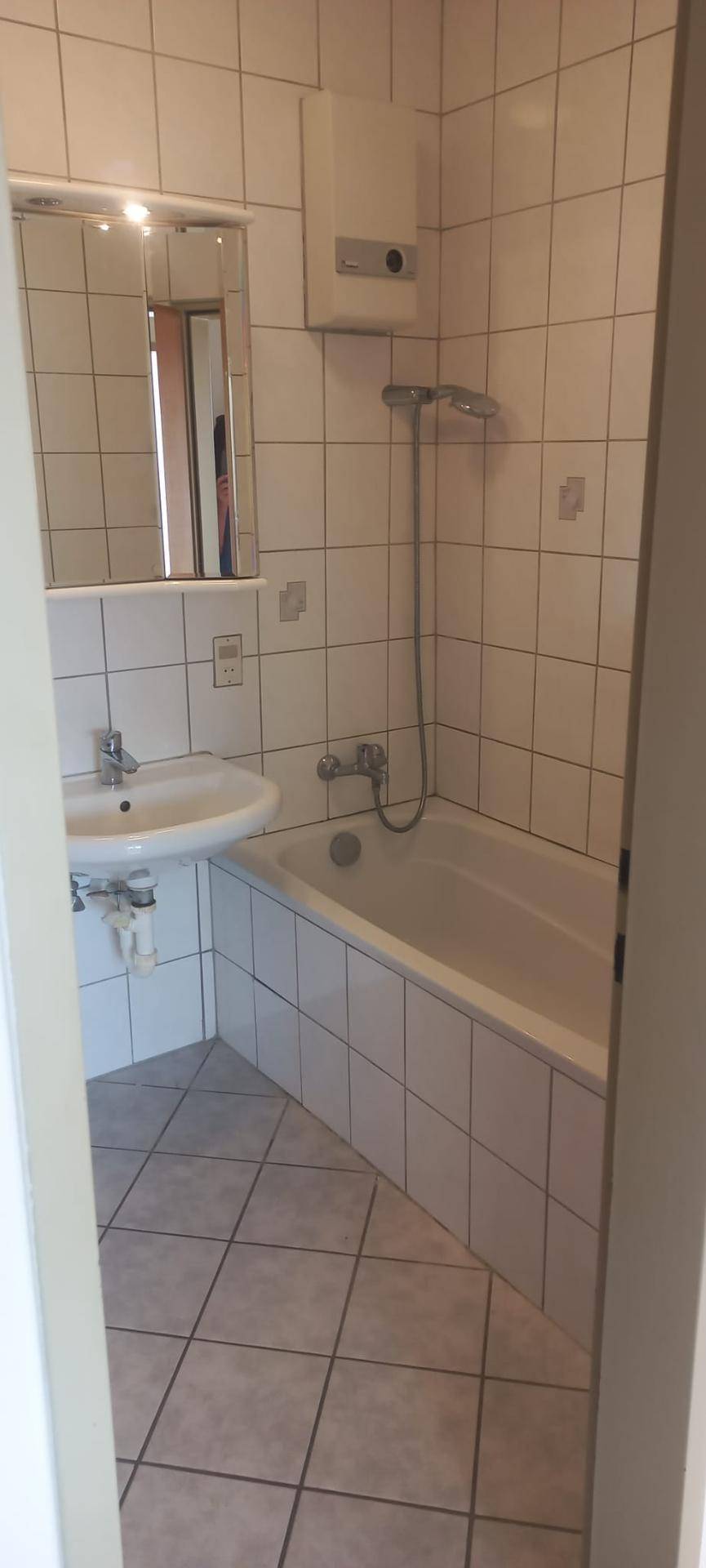 Gefliestes Badezimmer mit Badewanne, Waschbecken und Spiegel, in hellem Design.