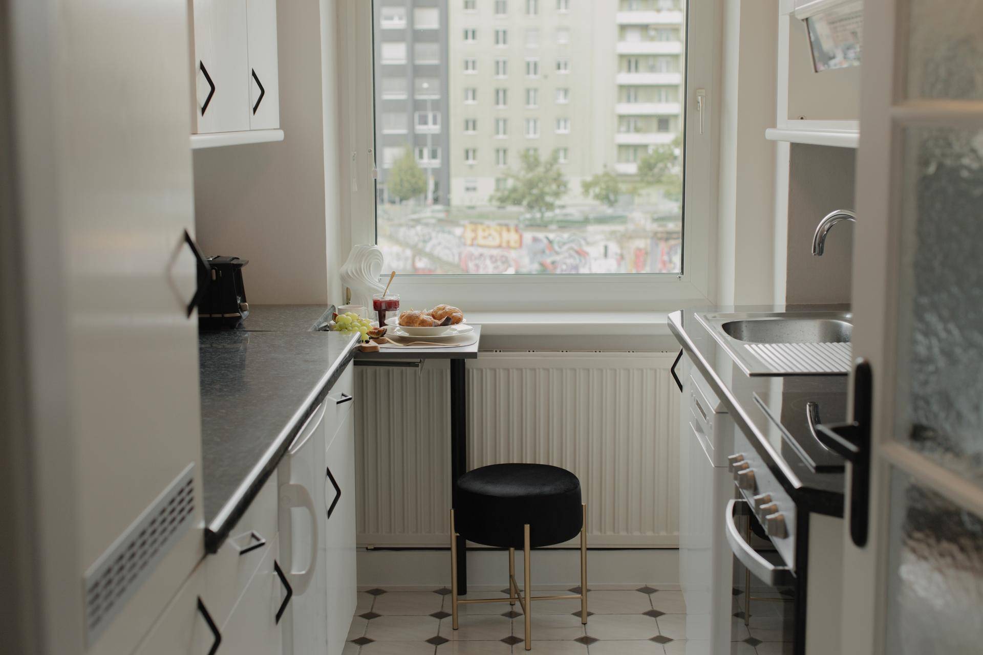 Kompakte Küche mit kleinem Esstisch am Fenster und Blick auf die umliegenden Gebäude.