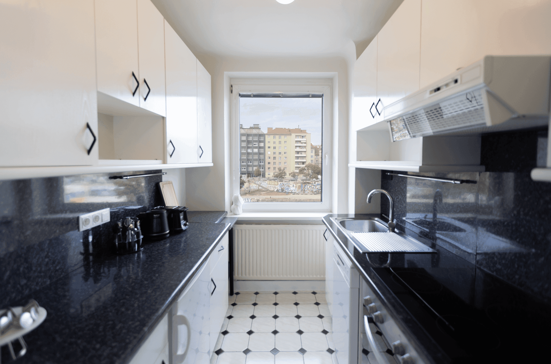 Funktionale Küche mit weißen Schränken, schwarzen Arbeitsplatten und Blick auf die Stadt.
