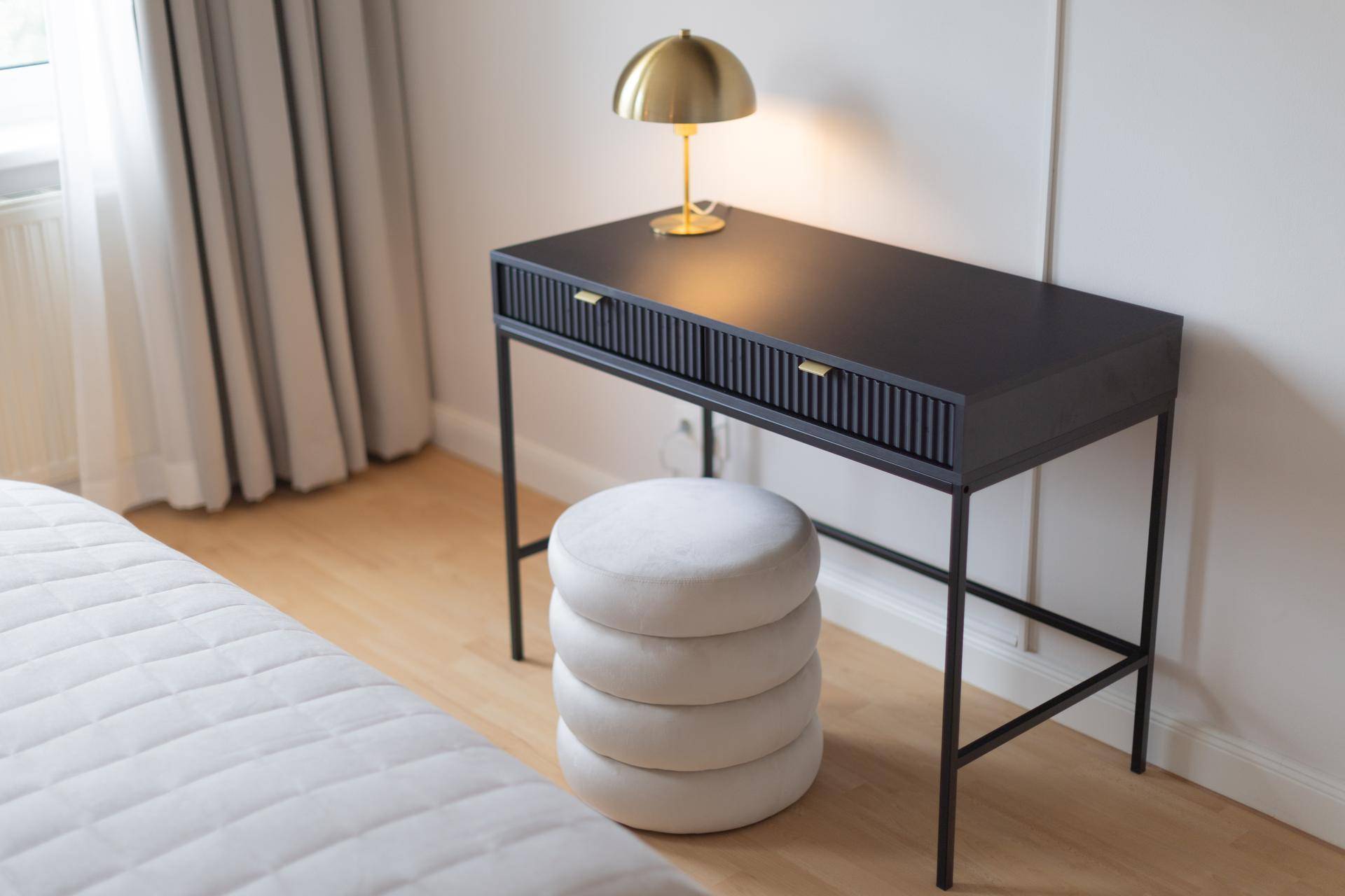 Moderner schwarzer Schreibtisch mit goldener Lampe und einem runden Hocker im Schlafzimmer.