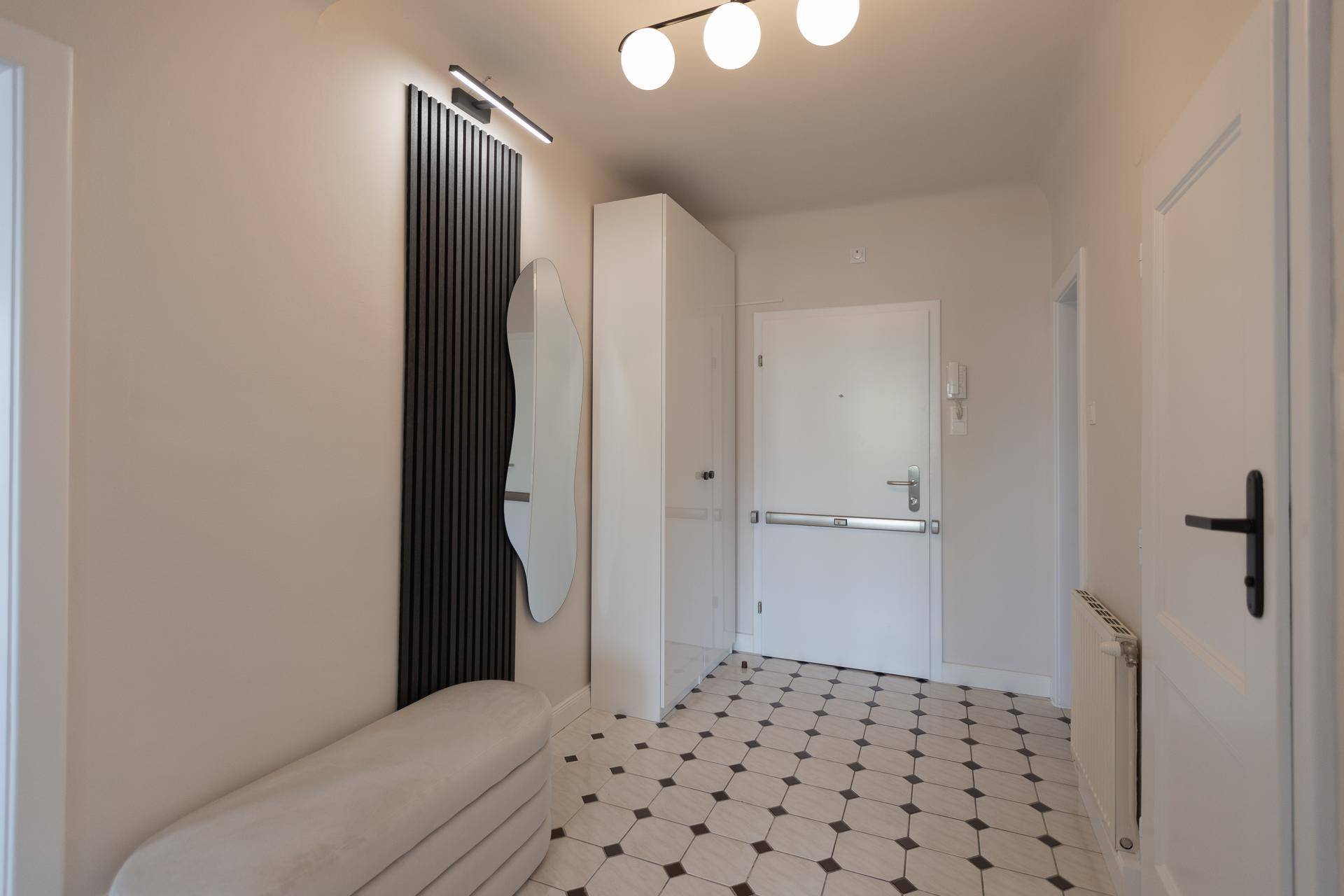 Heller Eingangsbereich mit gemusterten Fliesen, Garderobe und moderner Beleuchtung.