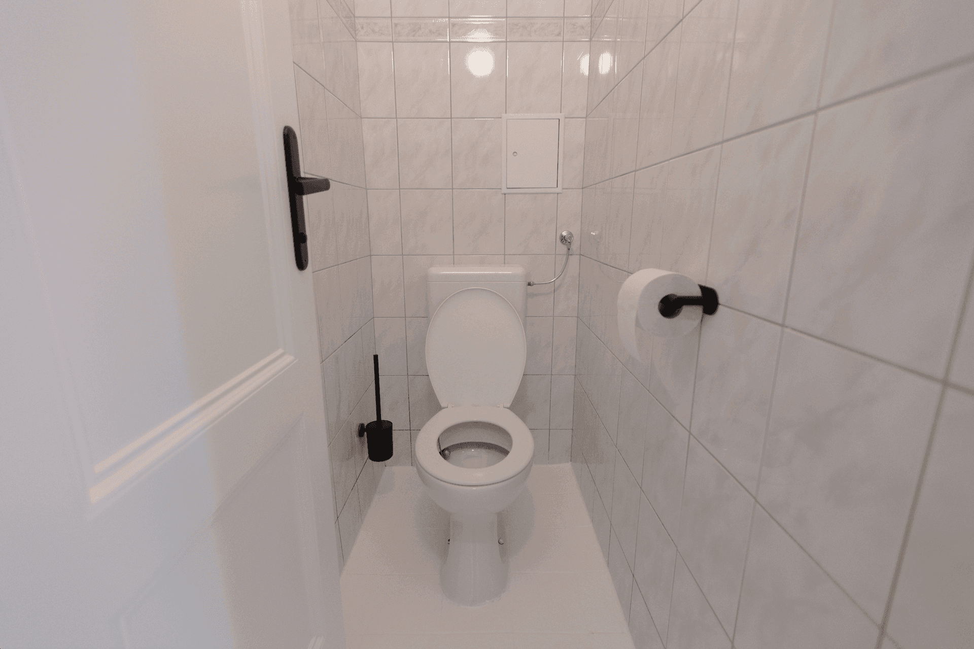 Separates WC mit weißen Fliesen und wandmontierter Toilette.